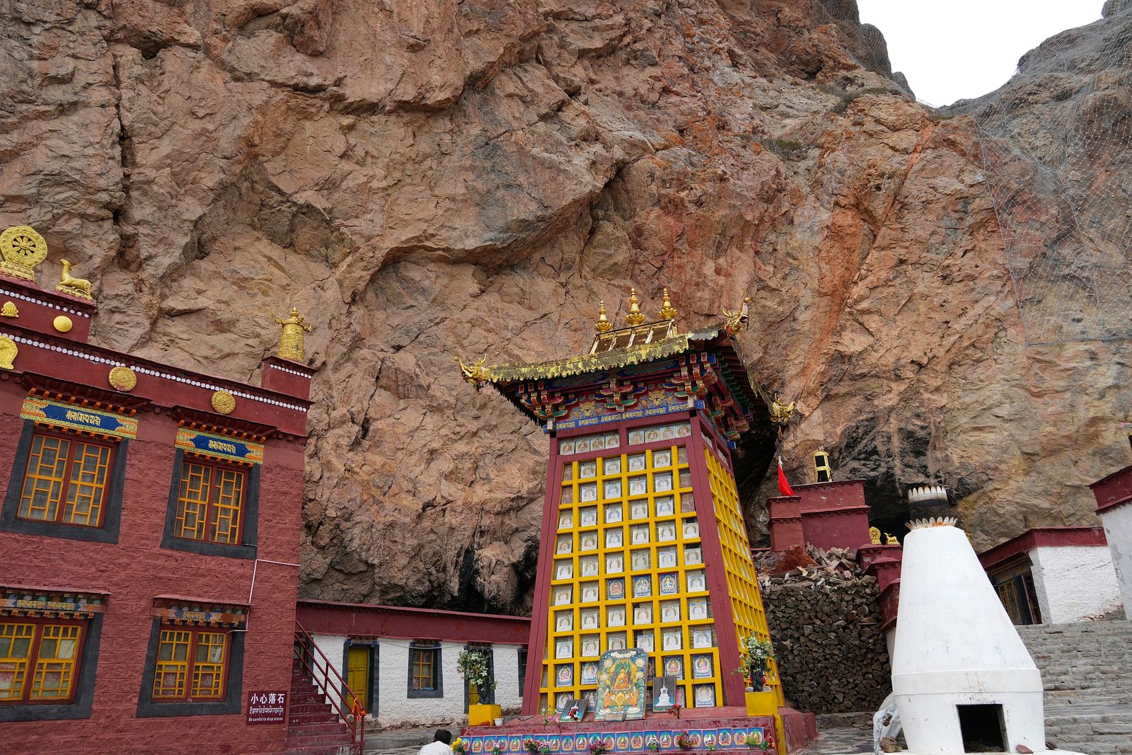 A red and yellow shrine beneath a steep rock face, Tibetan plateau