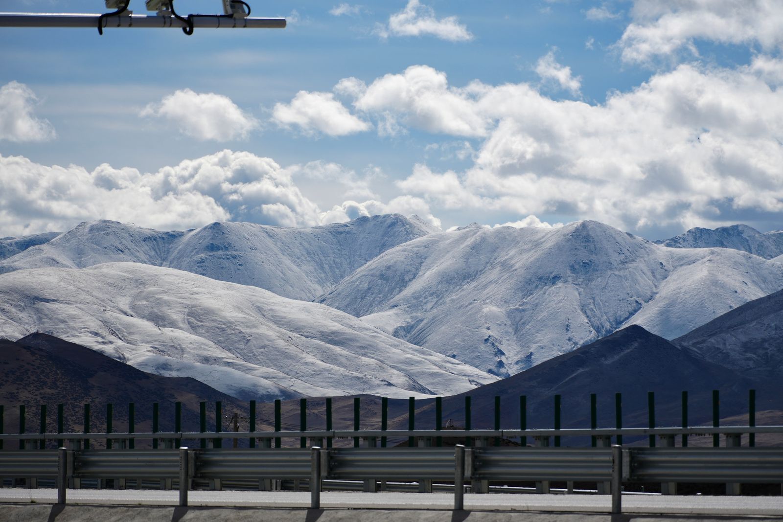 Snow-covered mountains beyond dark slopes and road barriers, Tibetan plateau