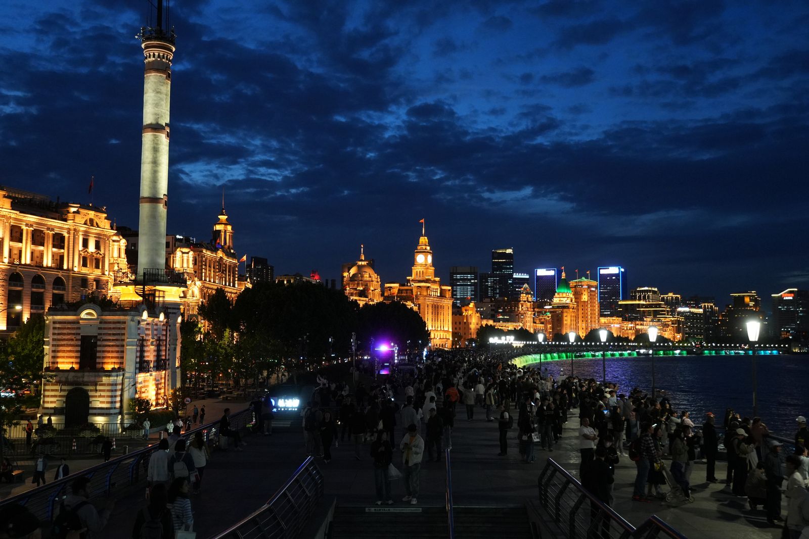 Gold-lit waterfront buildings beside a crowded promenade at dusk, Shanghai