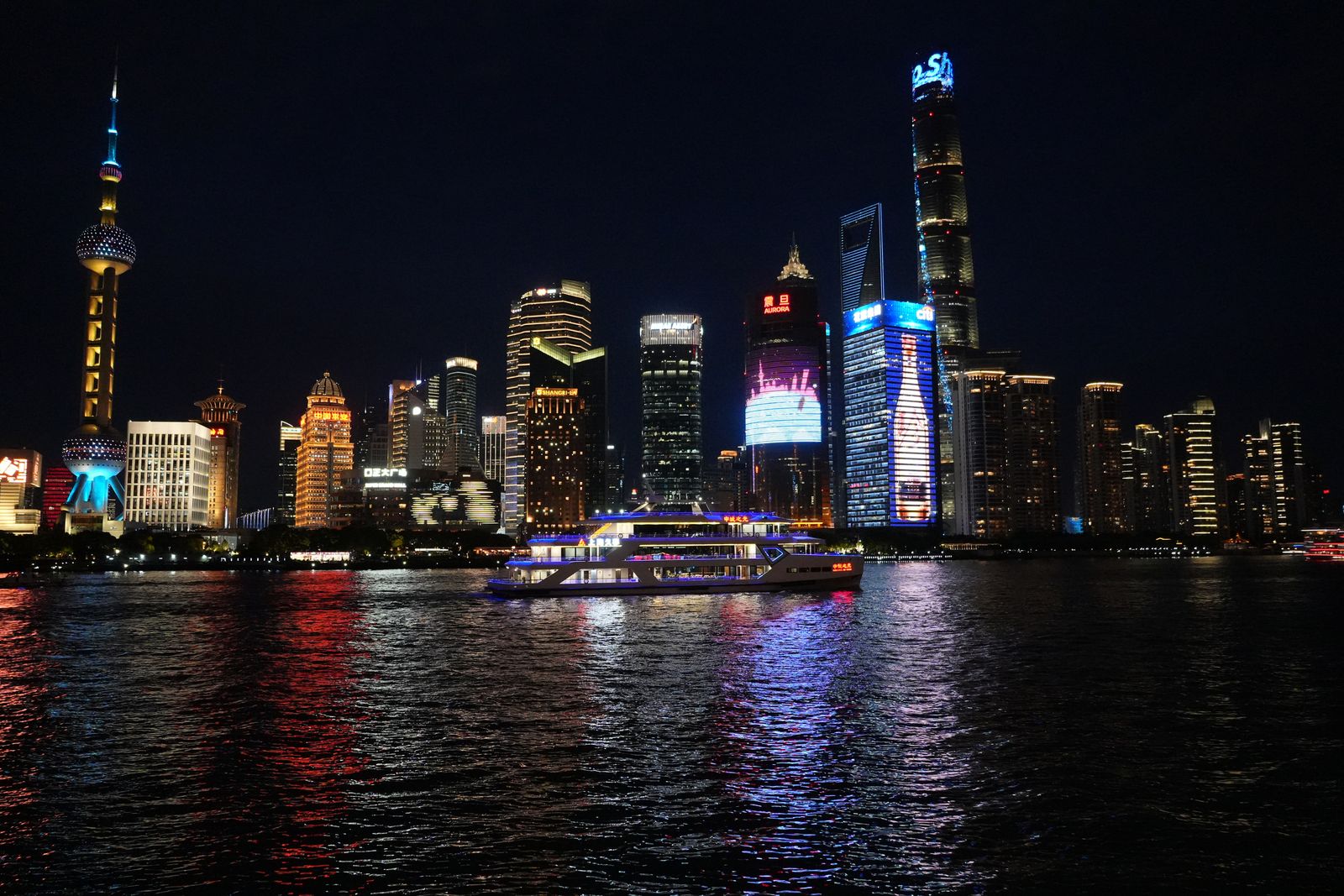 Shanghai skyline across a river with a boat at night