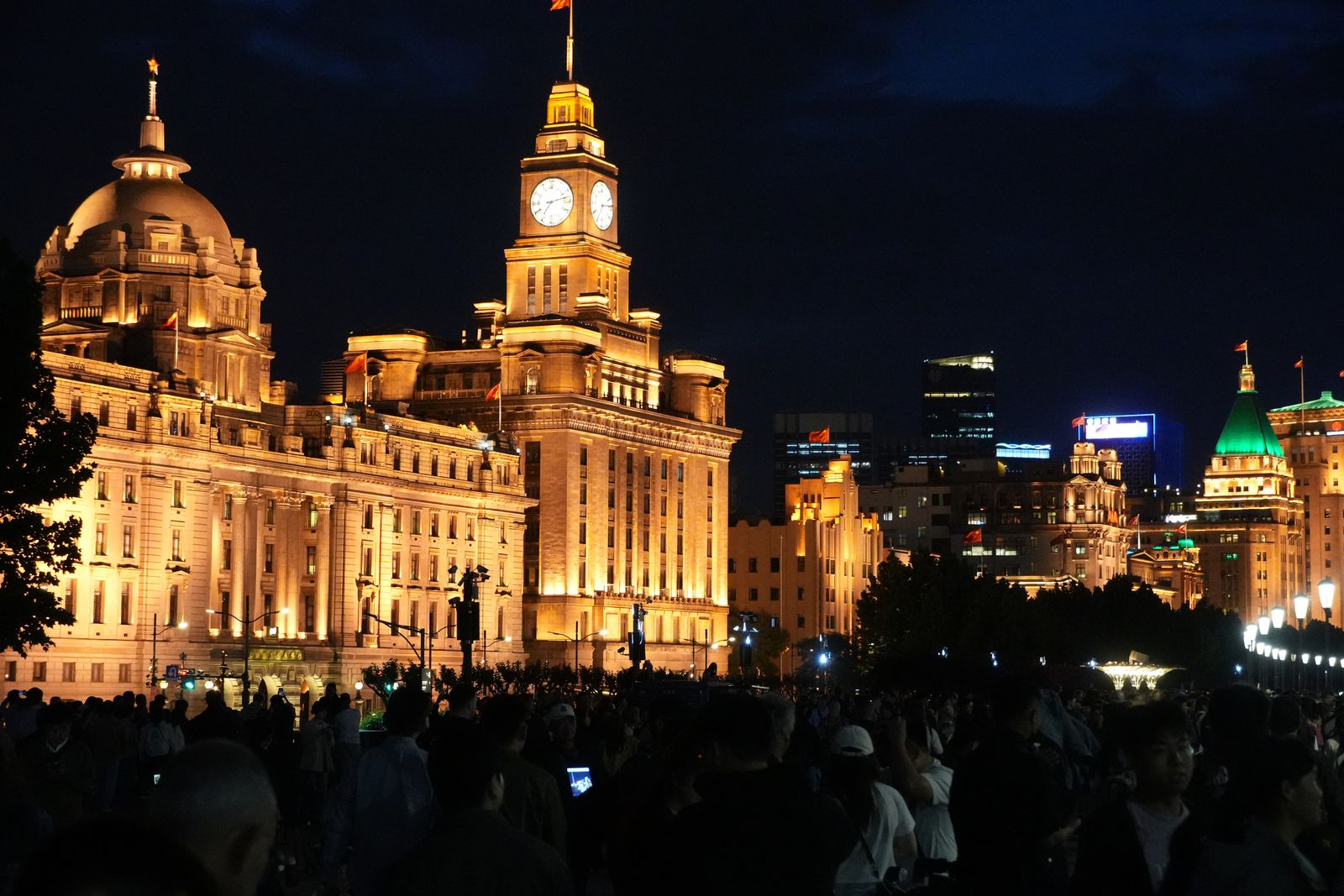 Waterfront buildings and a clock tower above crowds at night, Shanghai