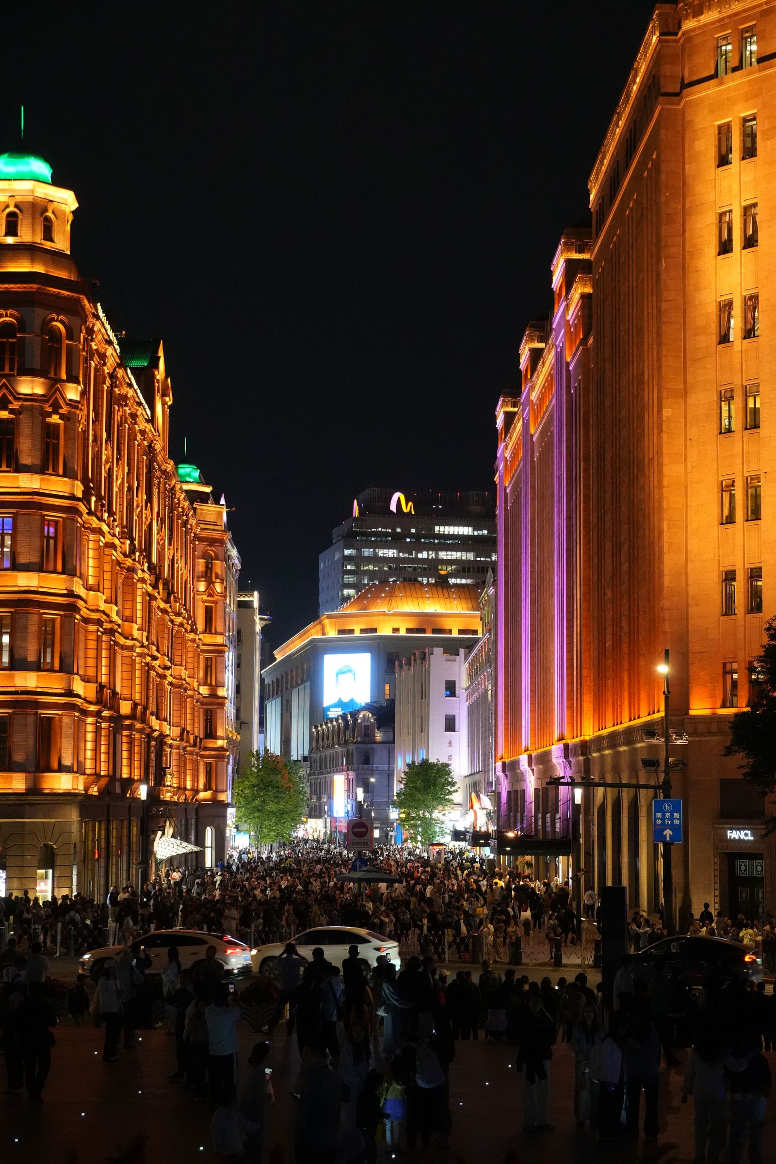 A crowded Shanghai street with gold-lit buildings at night