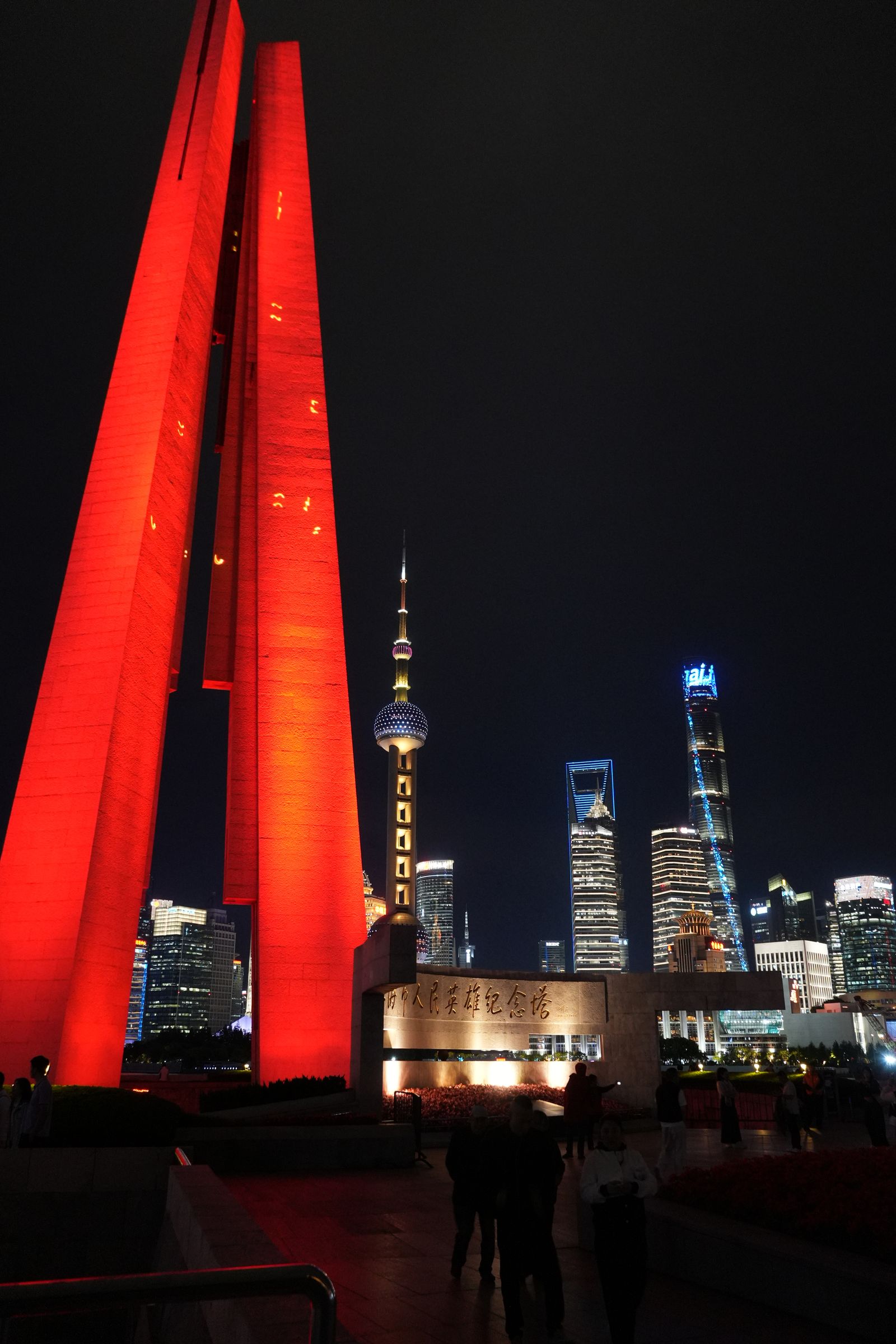 A red-lit monument beside the Shanghai skyline at night