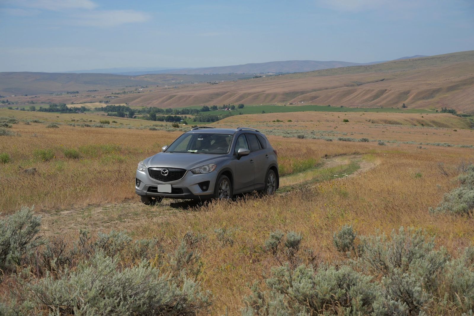 A silver SUV on a dirt track amid rolling hills, shrub-steppe
