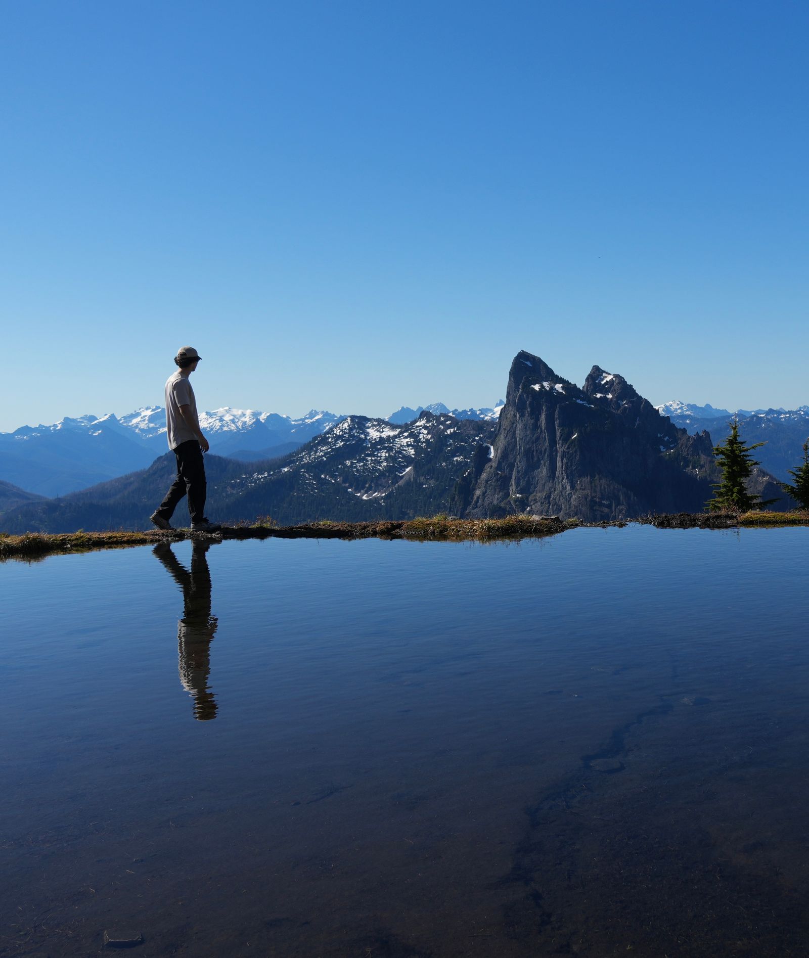 A person reflected in a tarn below rocky peaks, Gunn Peak