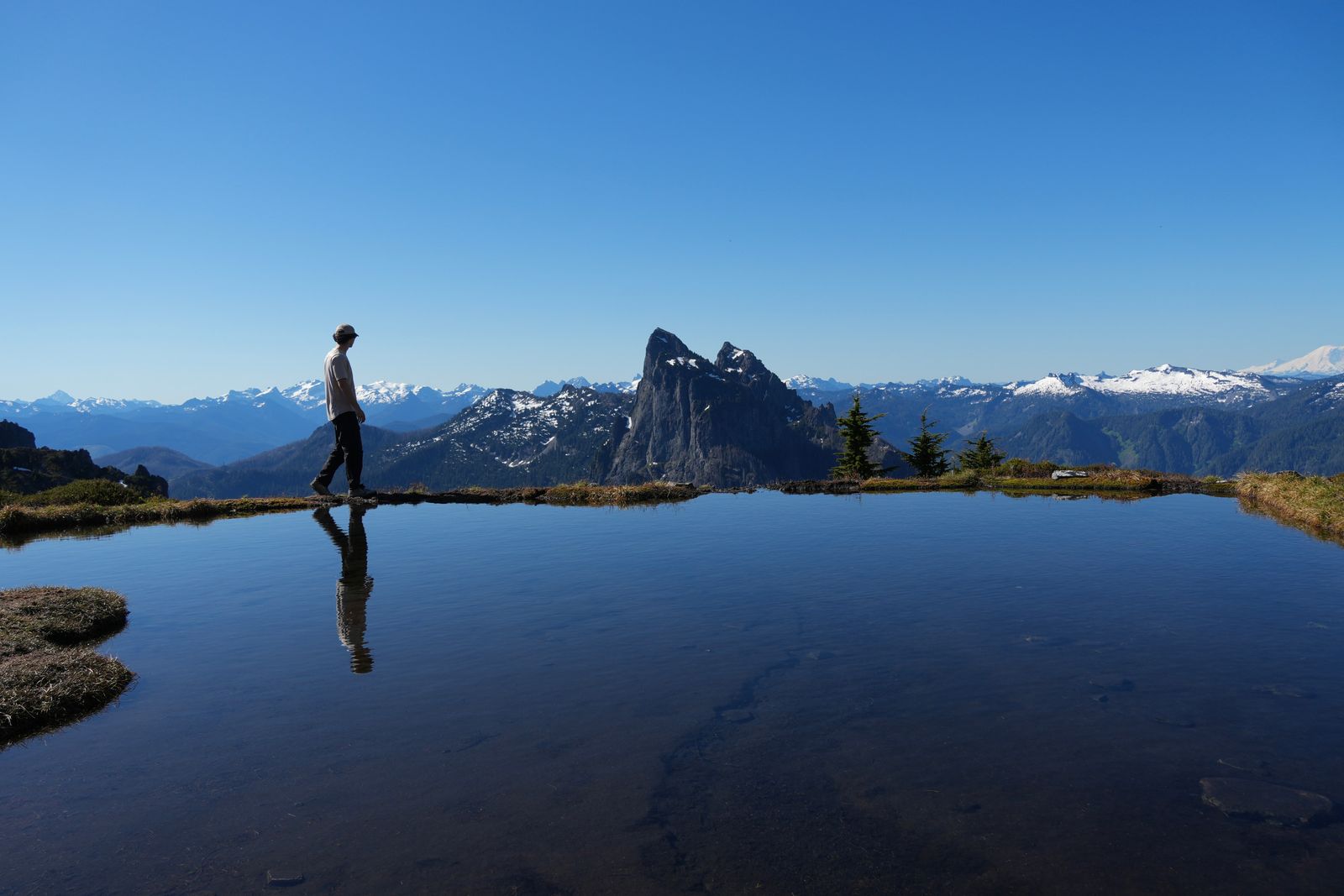 A person reflected in a tarn below rocky peaks, Gunn Peak
