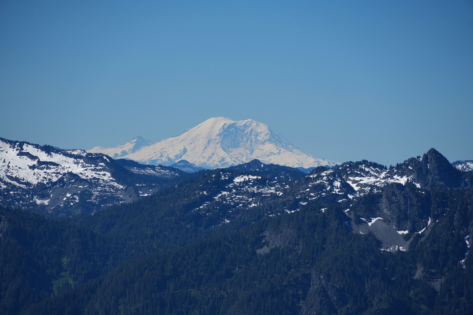 A snow-covered peak beyond forested ridges and rocky outcrops, Gunn Peak