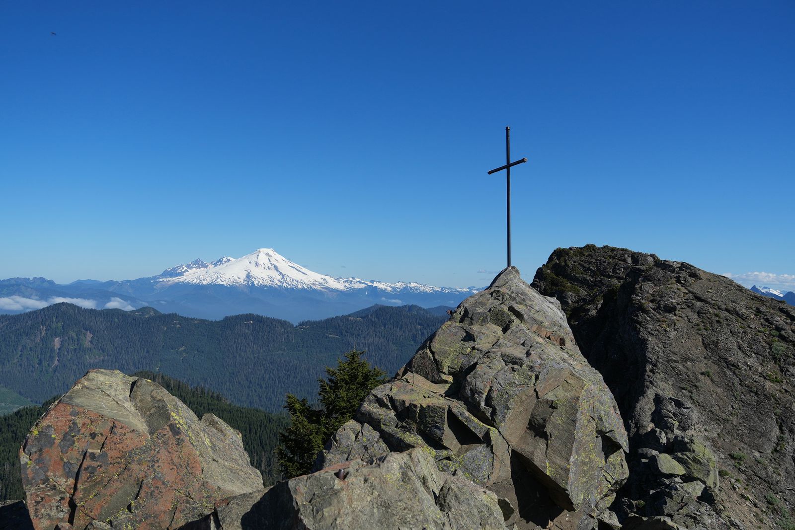 Metal cross on a rocky summit above forested ridges, Sauk Mountain