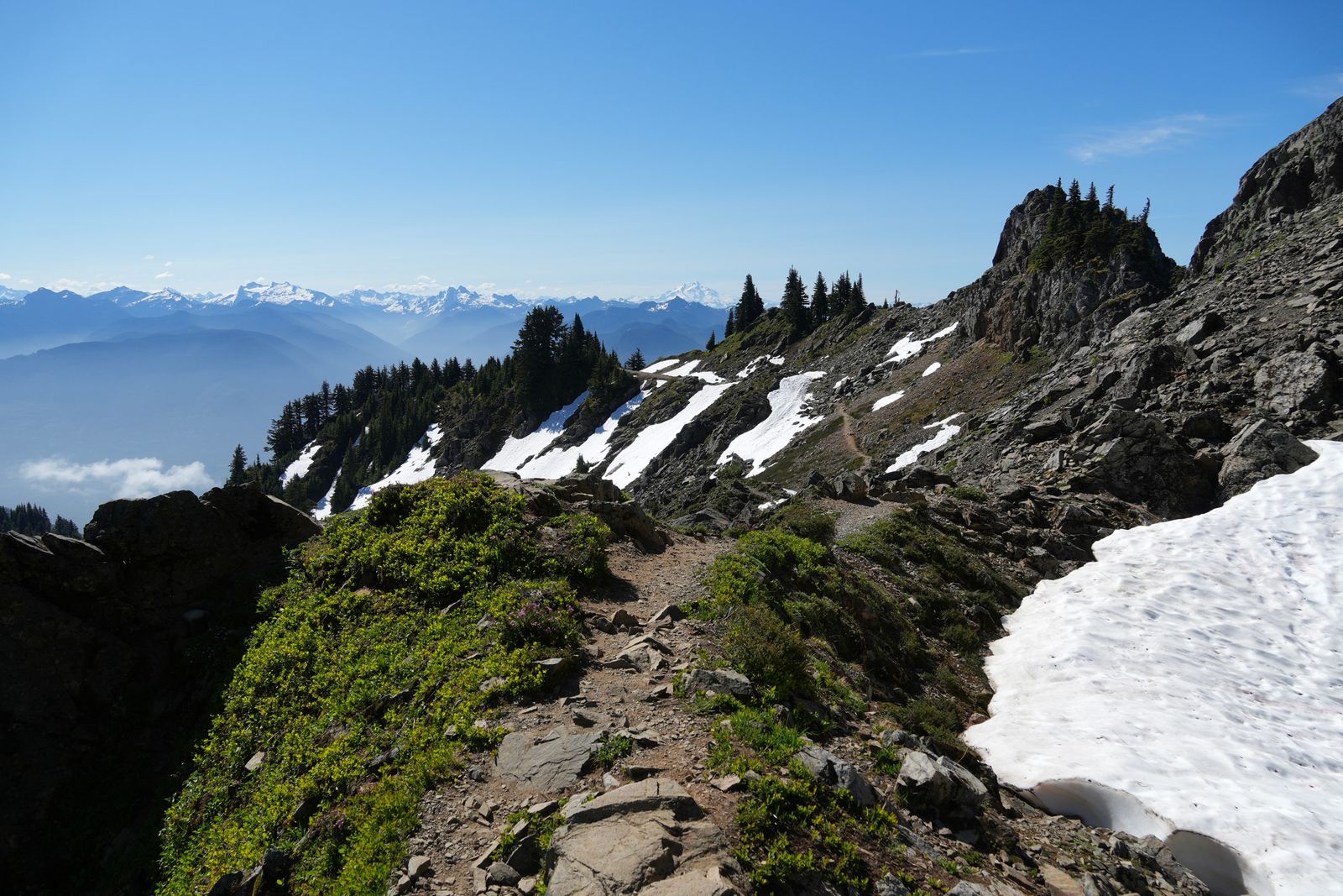 Rocky mountain trail crossing patches of snow below jagged rocks, Sauk Mountain