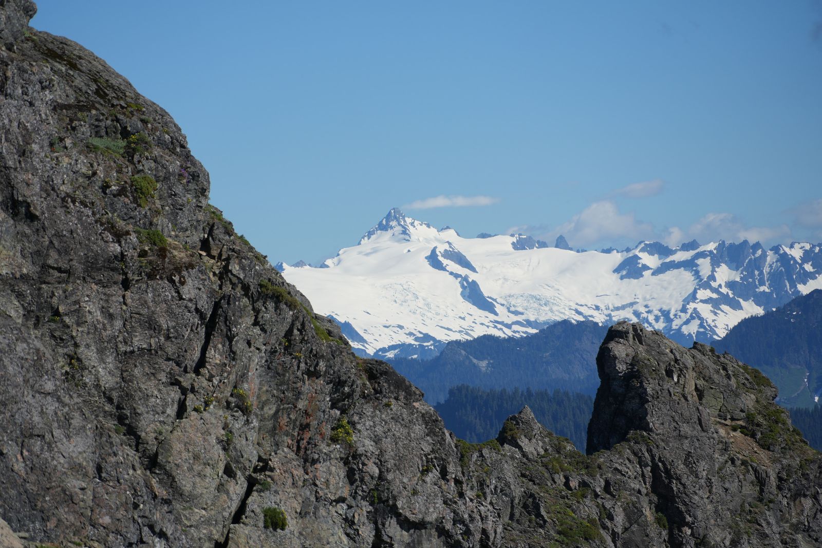 Snow-covered mountains beyond rocky outcrops and forested slopes, Sauk Mountain