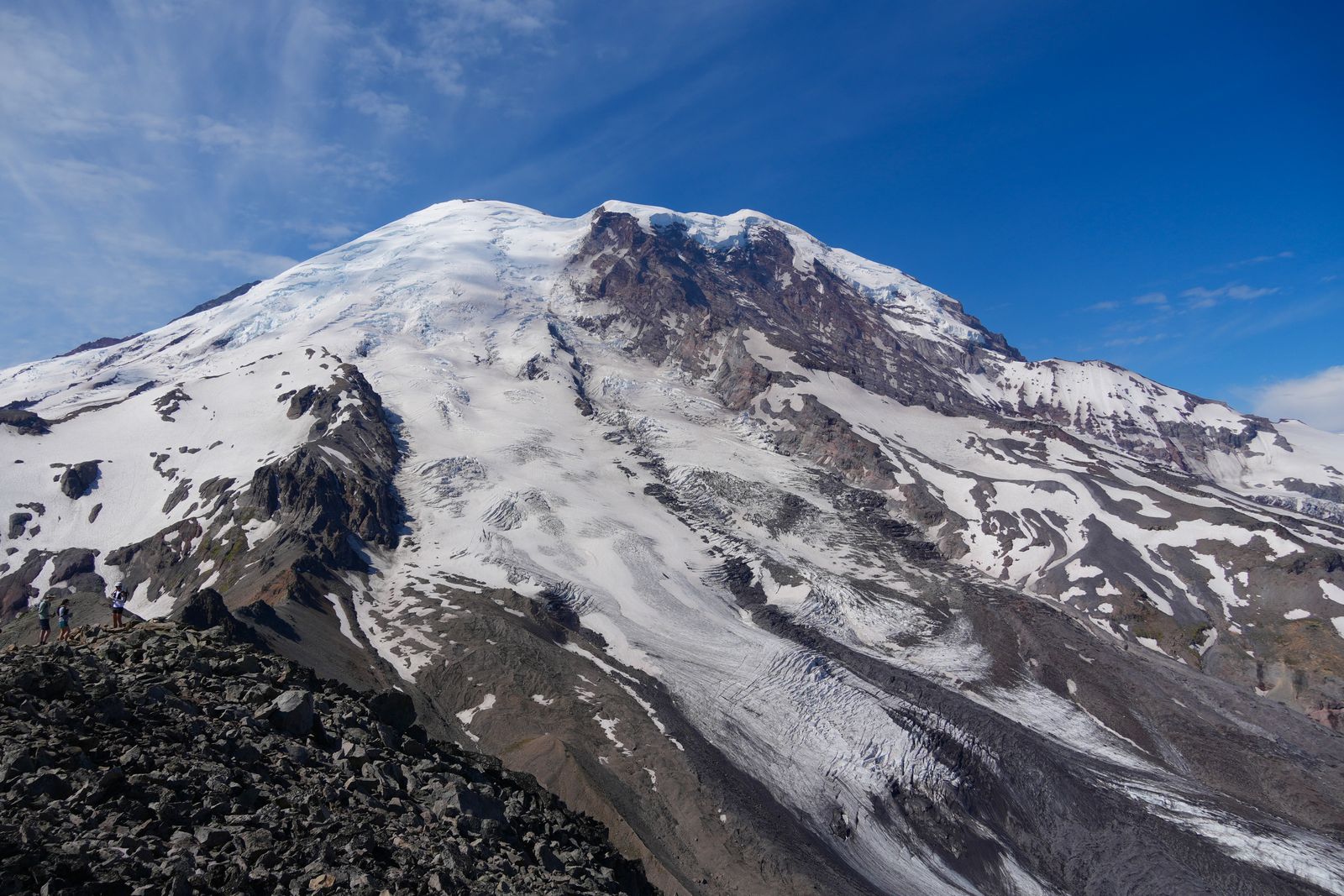 Mount Rainier above three people on a rocky ridge, Sunrise