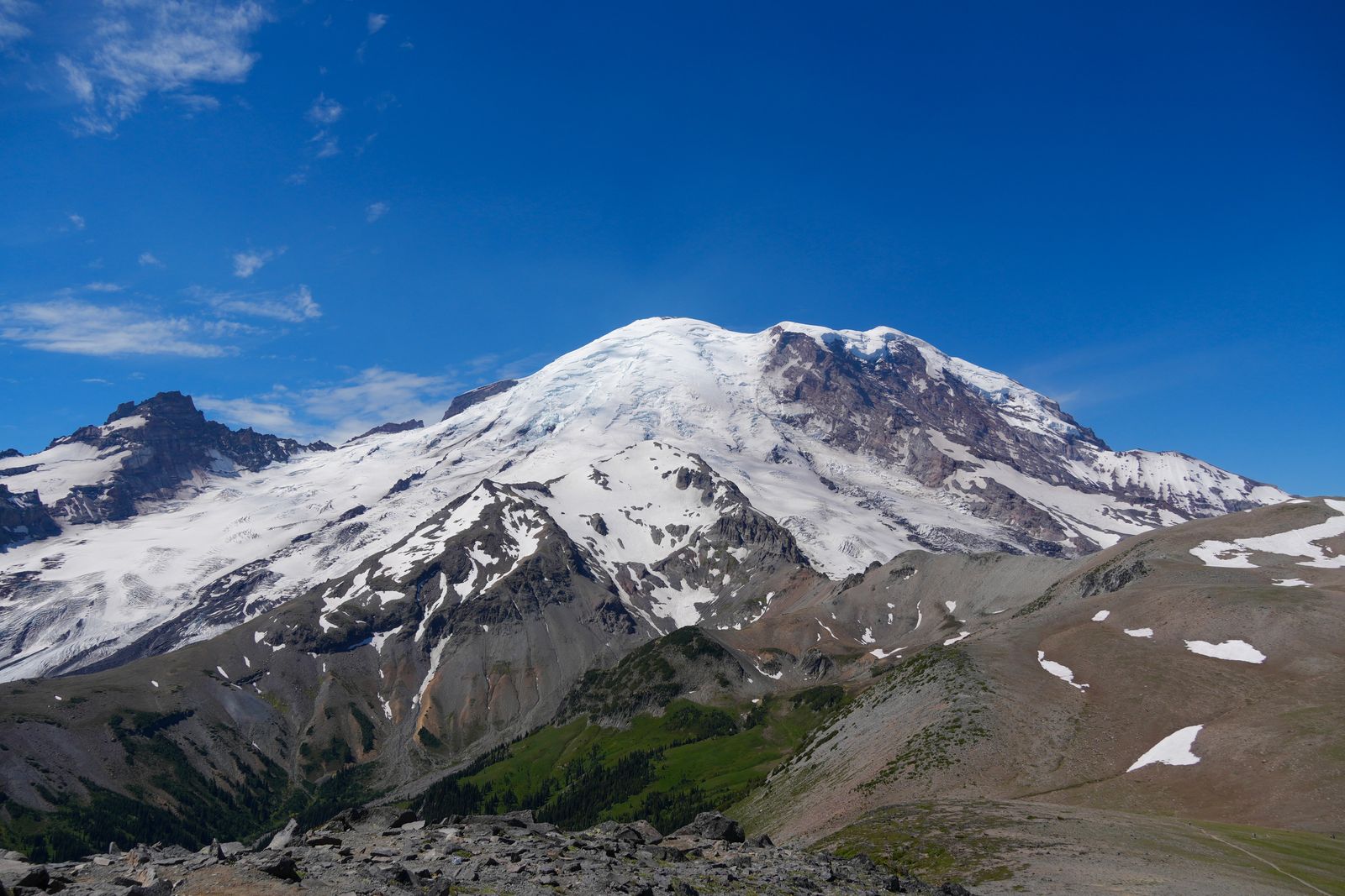 Mount Rainier above rocky slopes and a green valley, Sunrise