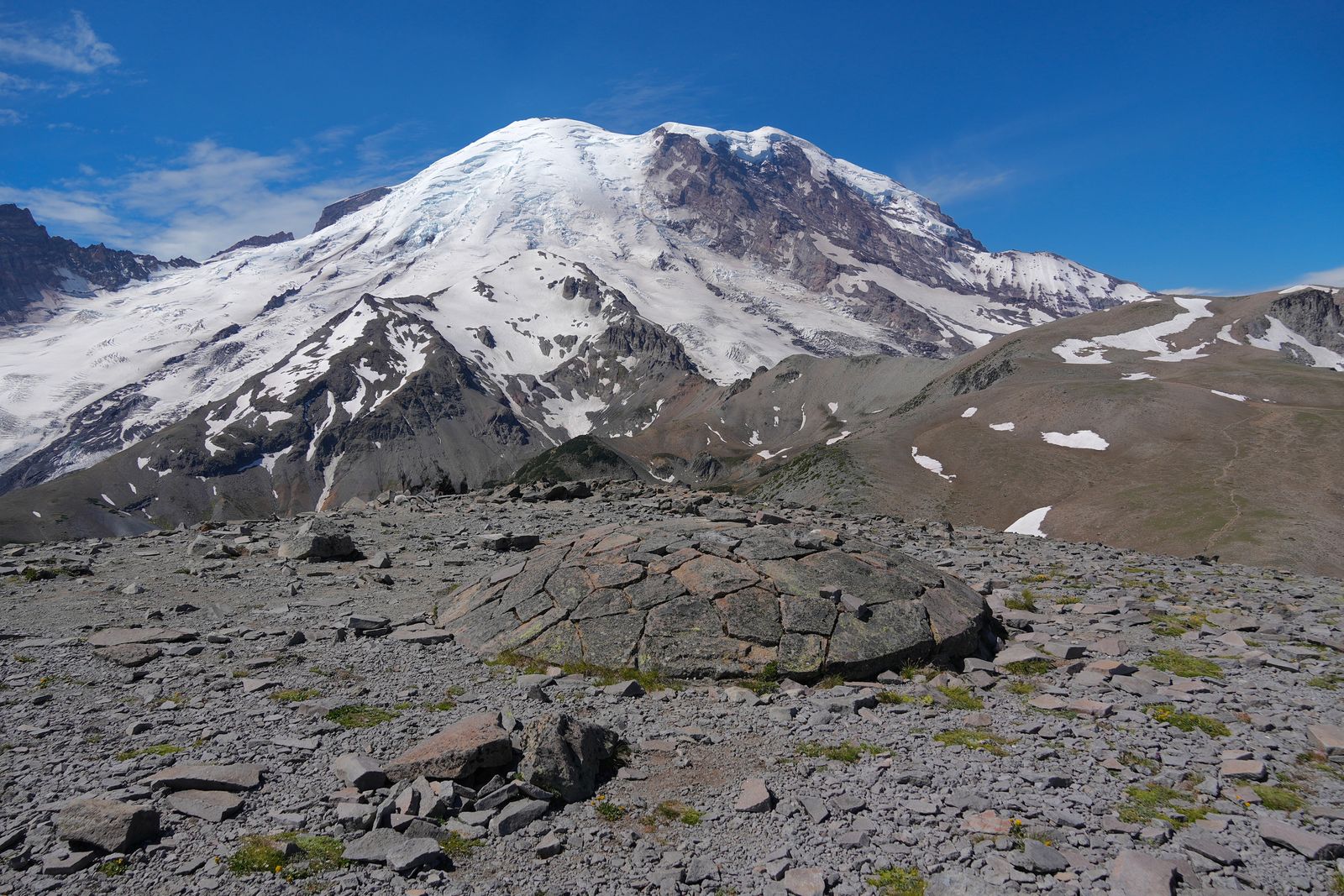 Mount Rainier beyond a cracked boulder and patchy snow, Sunrise