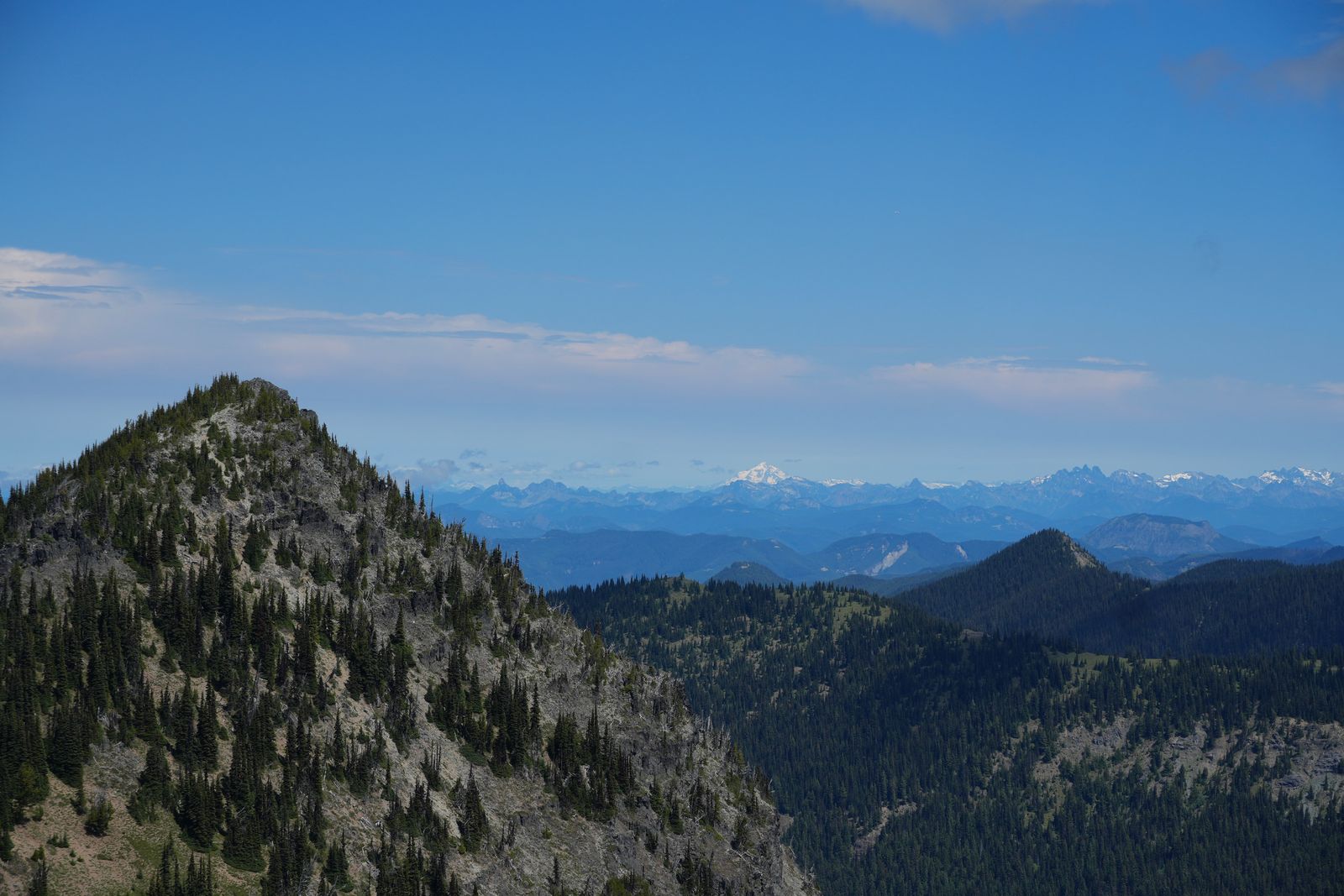 Rocky ridge above forested valleys below snow-covered peaks, Sunrise