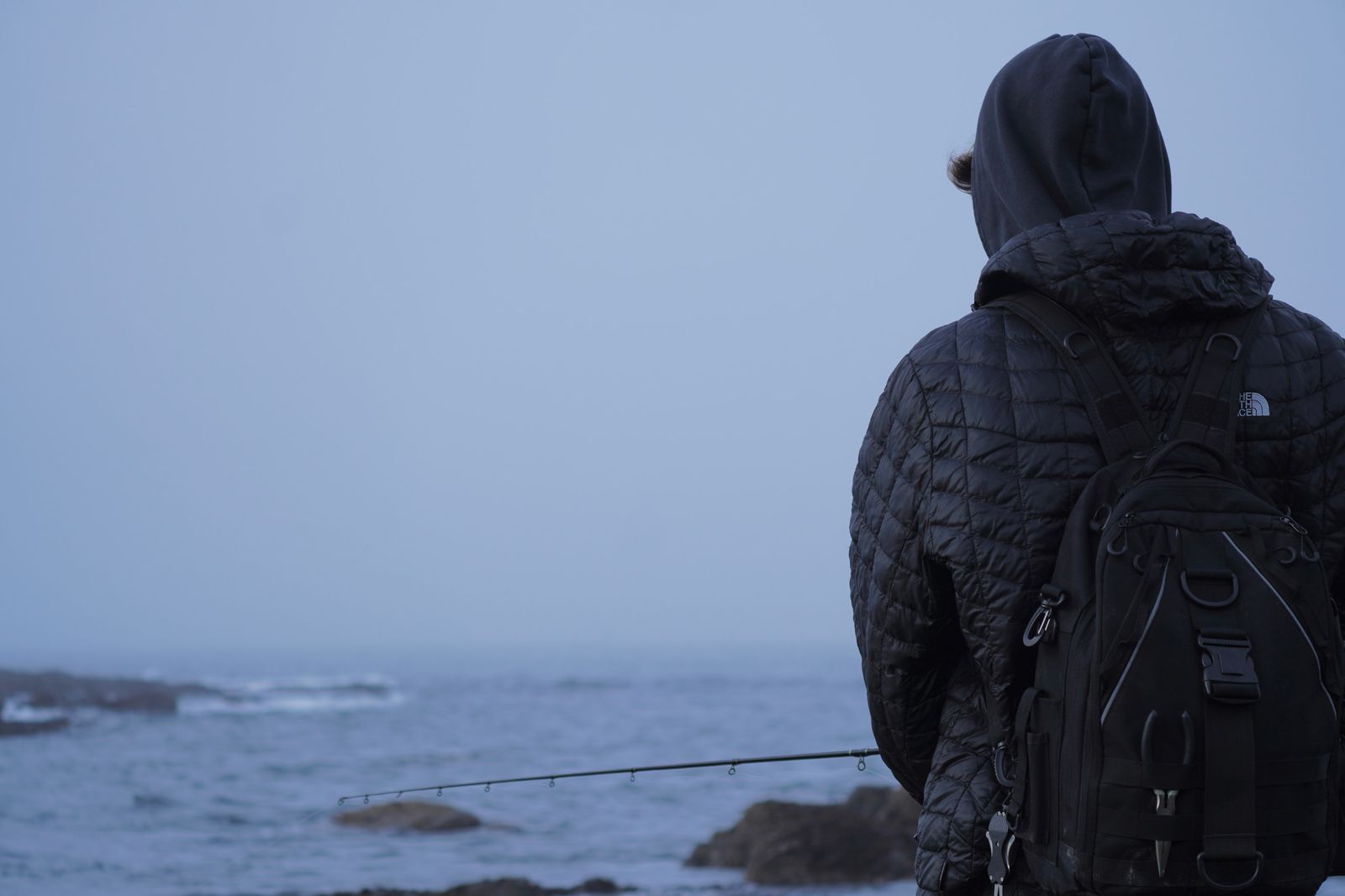 A hooded person fishing on a rocky shore in fog, Olympic National Park