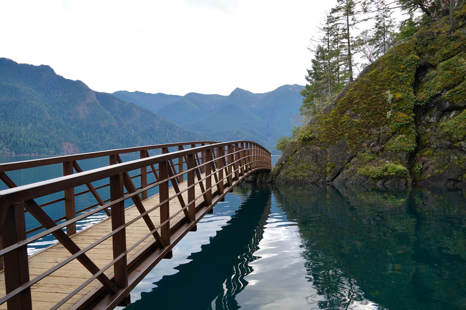 A footbridge curving over a lake beside mossy rocks, Olympic National Park