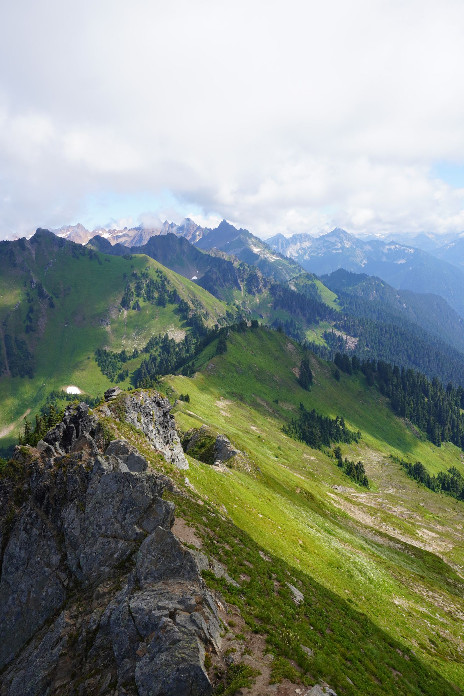 Green mountain ridges beyond a rocky crest under low clouds, North Cascades