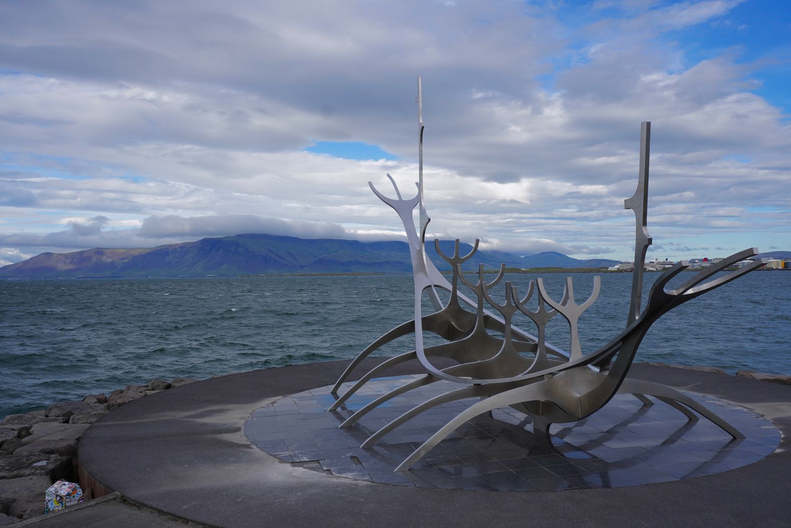 Boat-shaped metal sculpture beside water with mountains beyond, Reykjavik