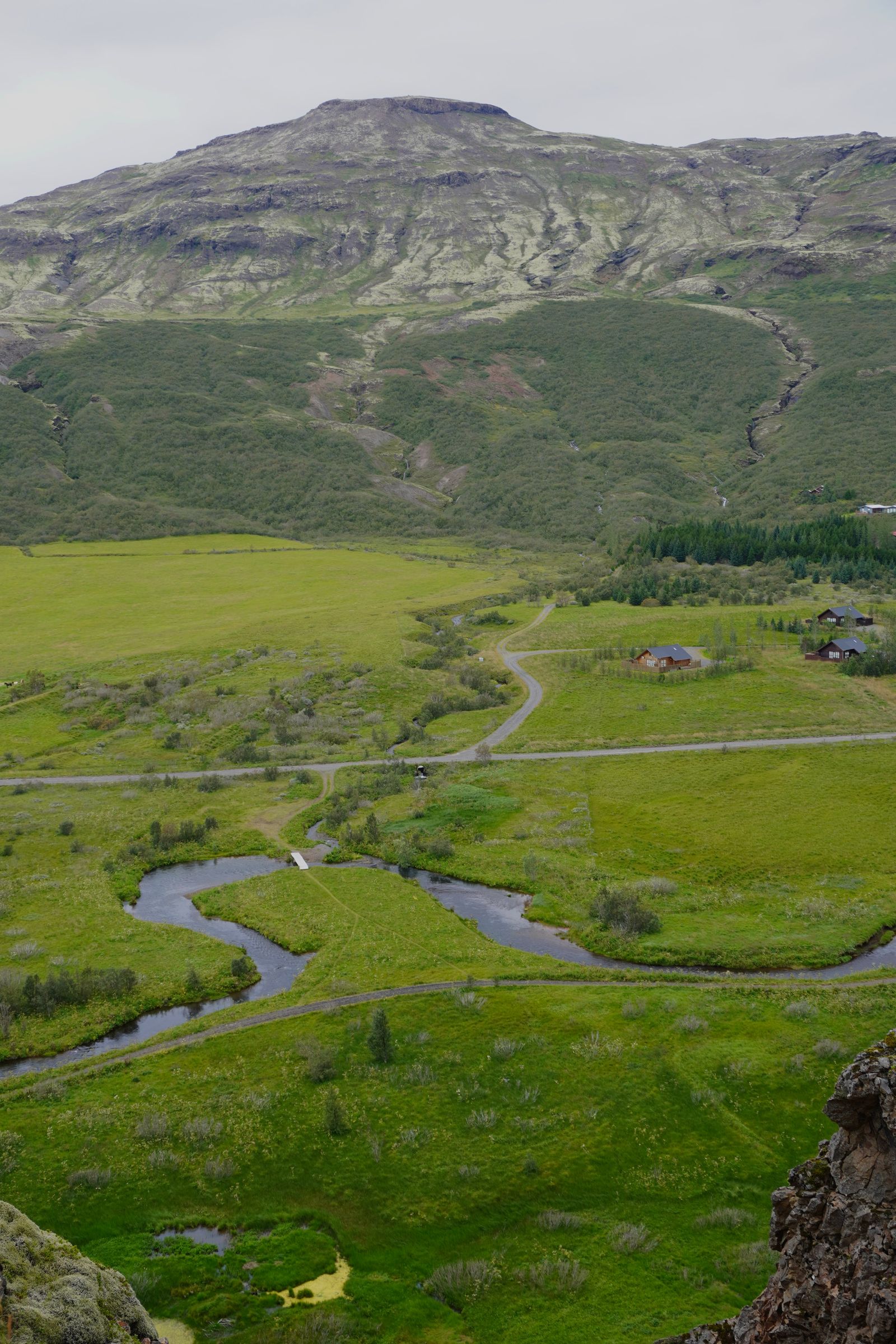 Rocky mountain above green fields and a winding stream, Bláskógabyggð