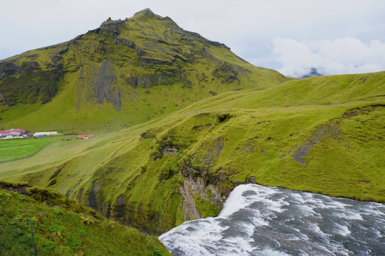 Skogafoss spilling over a rocky edge below green slopes