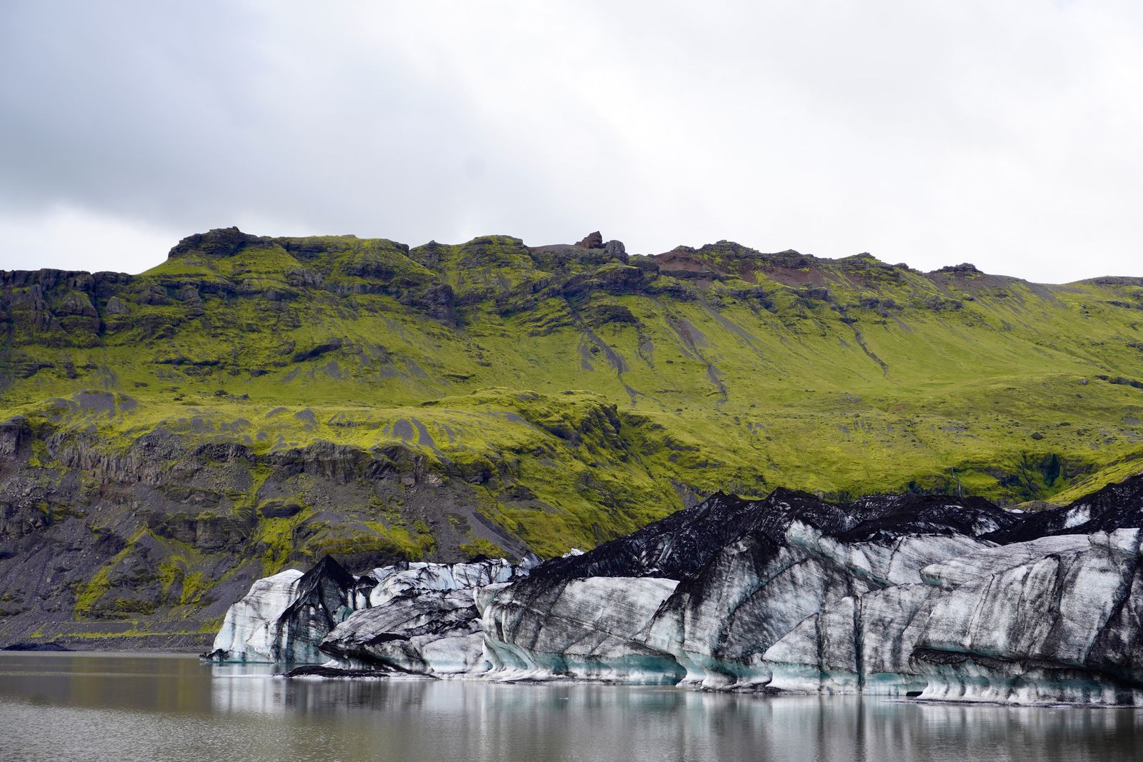 Glacier meeting a lake below green rocky slopes, Skogafoss
