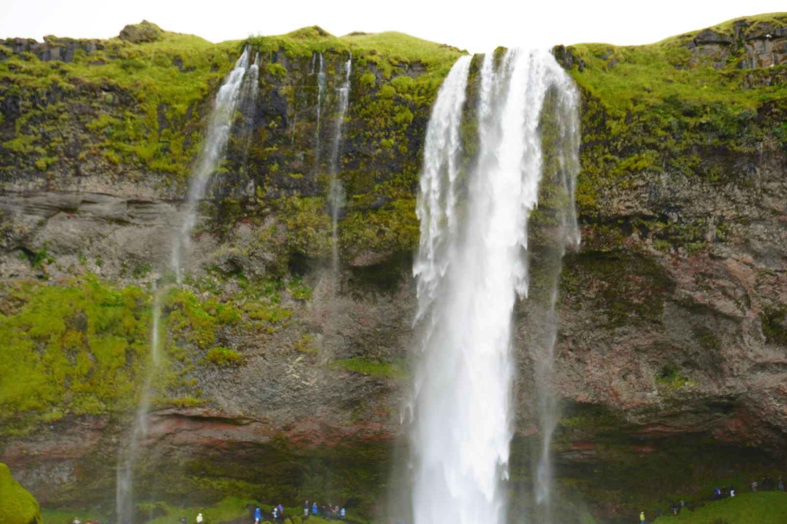 Waterfall cascading over a green-topped cliff with people below, Skogafoss