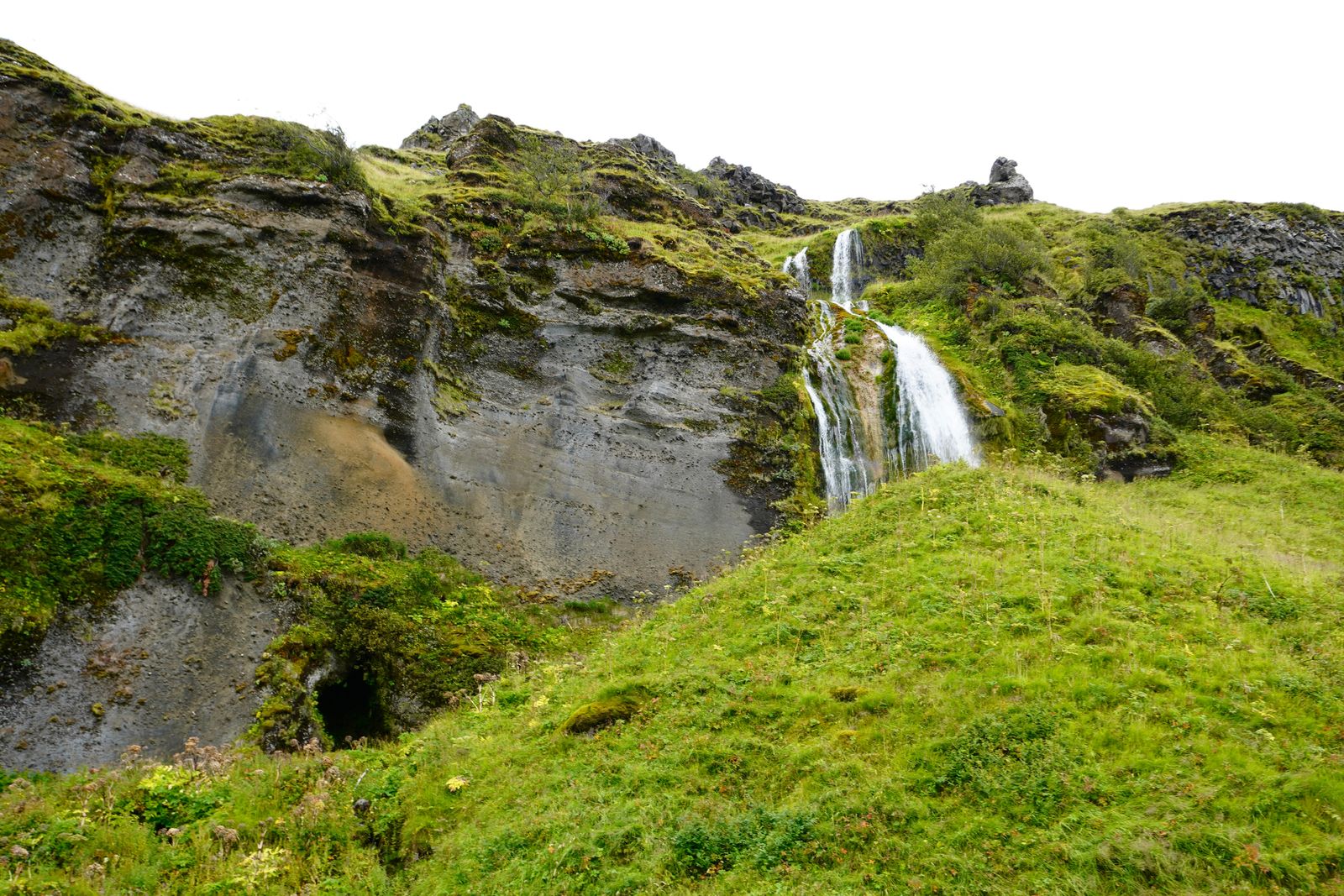 Waterfall cascading down rocky ledges above a grassy slope, Skogafoss