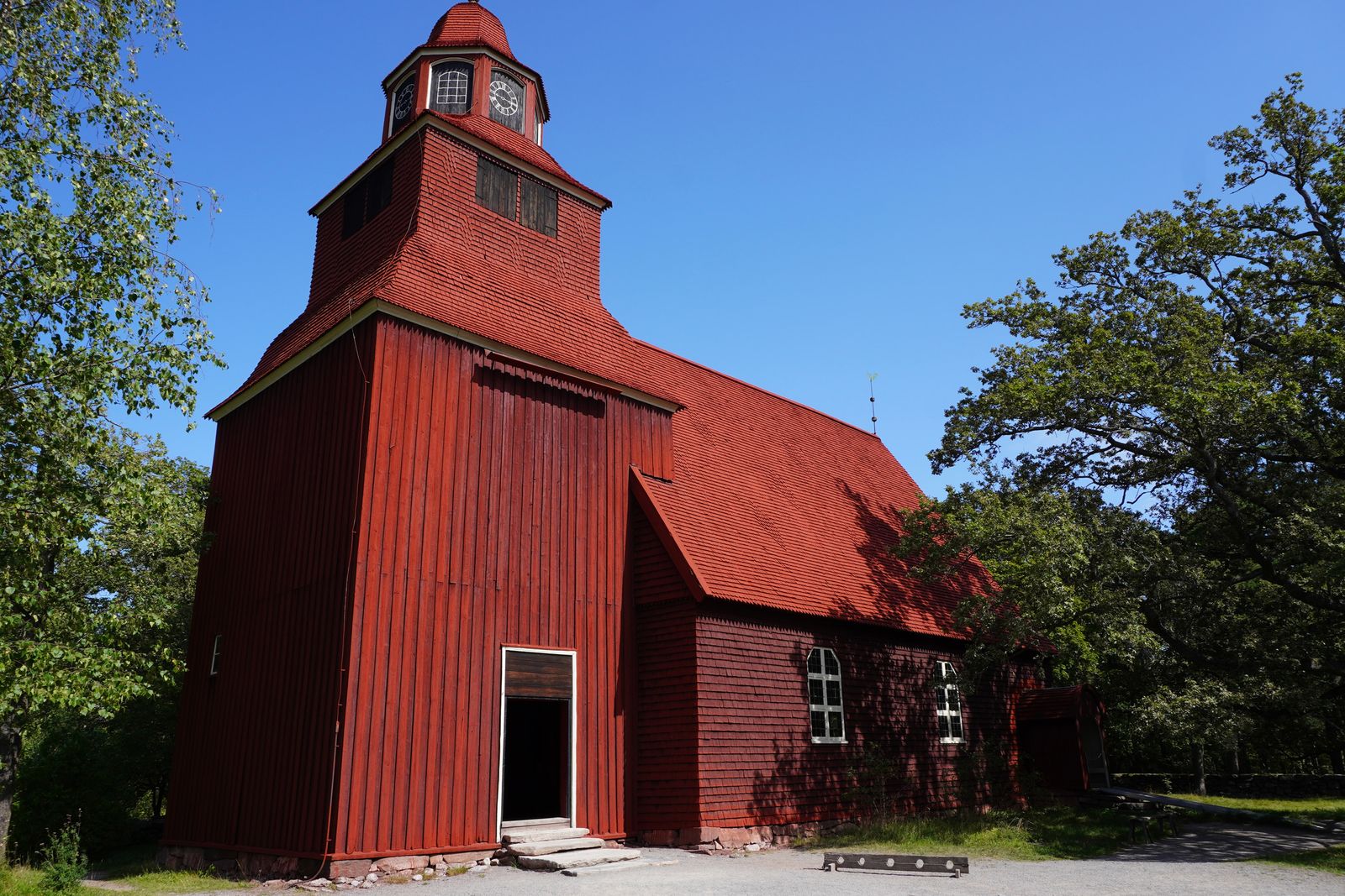 Red wooden church with an open doorway among leafy trees, Stockholm