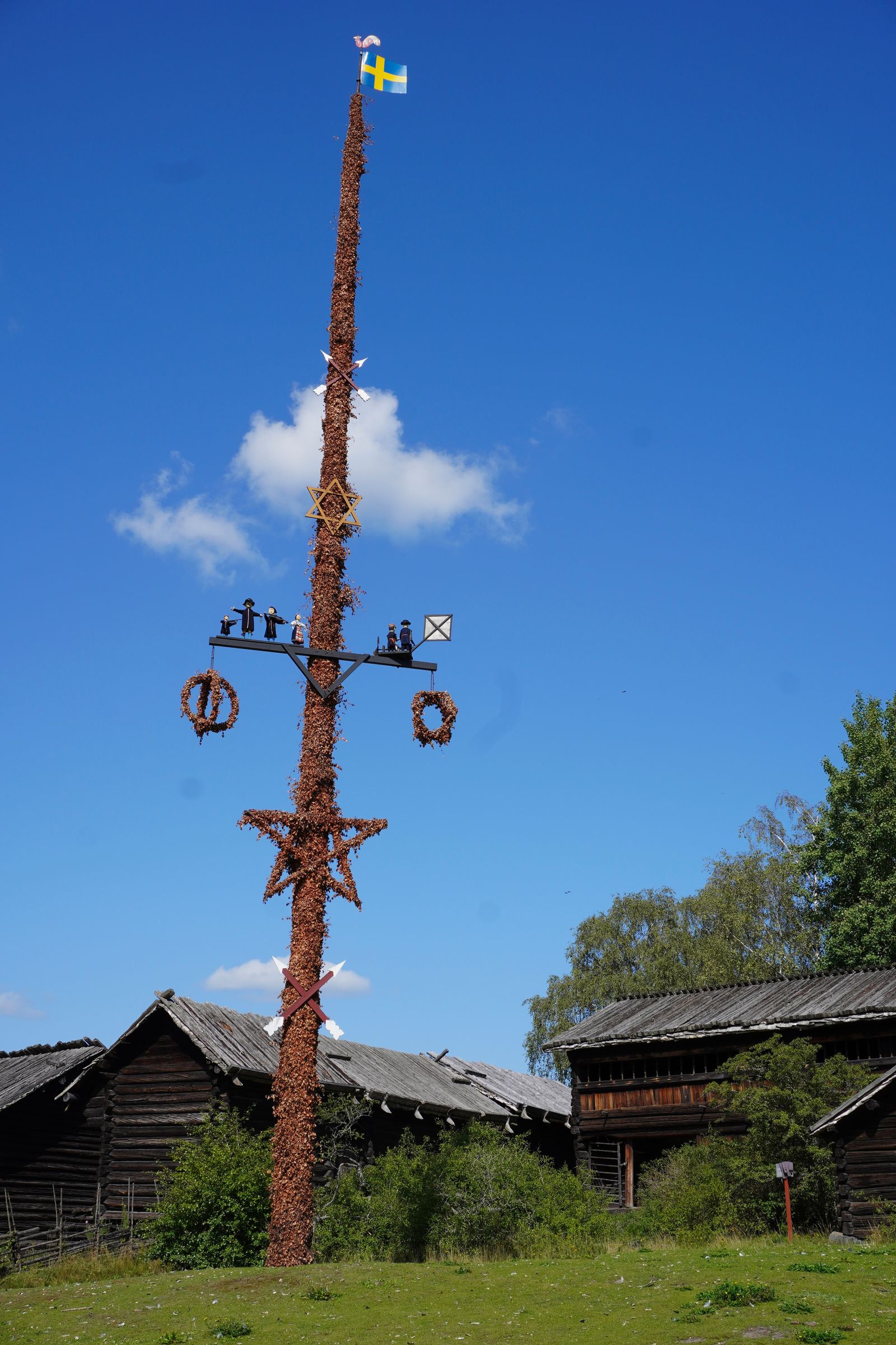 Decorated pole standing on grass in front of wooden buildings, Stockholm