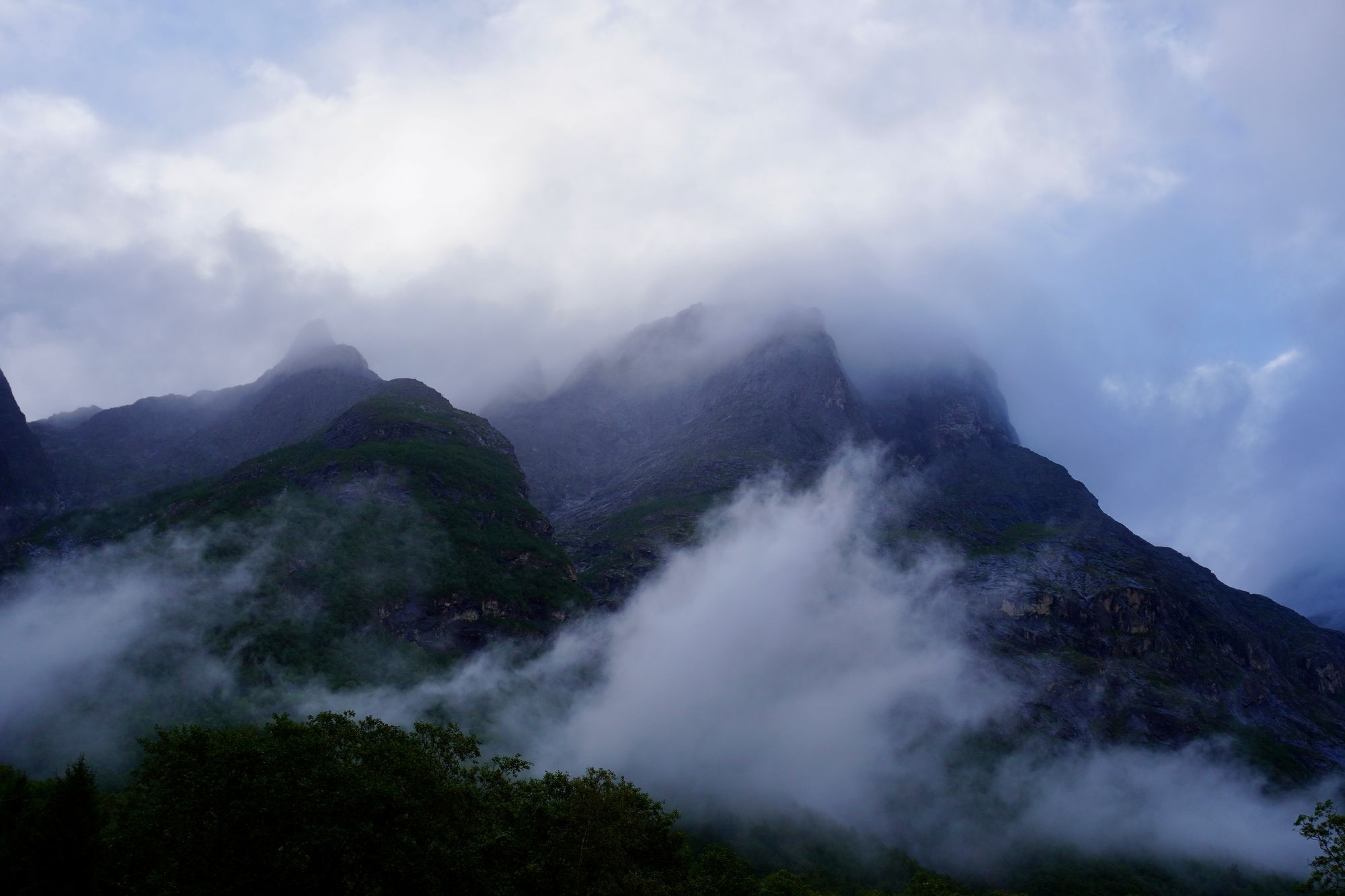 Rocky peaks above green slopes and trees in fog, Trollstigen