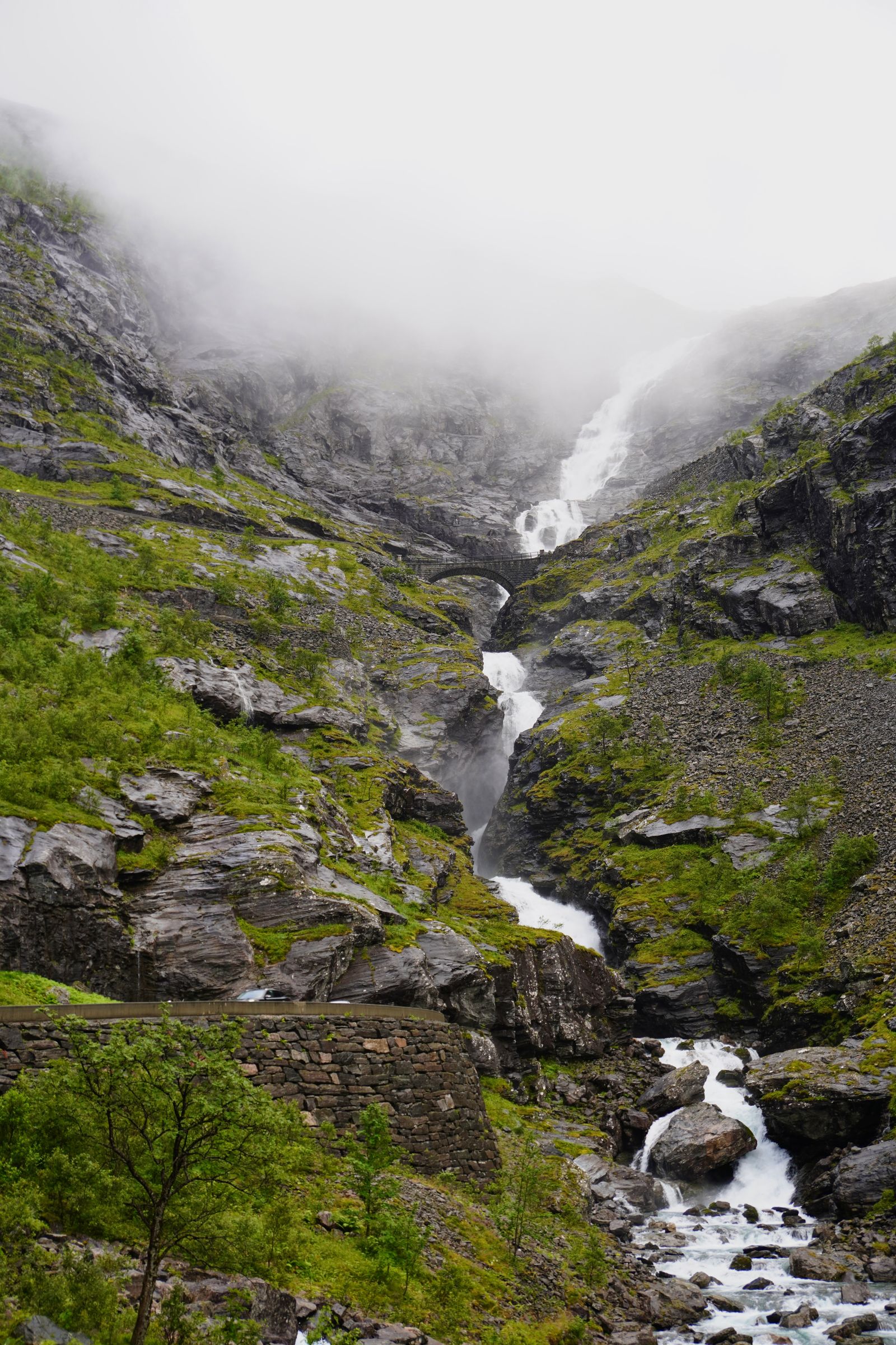 Waterfall beneath a stone bridge in fog at Trollstigen