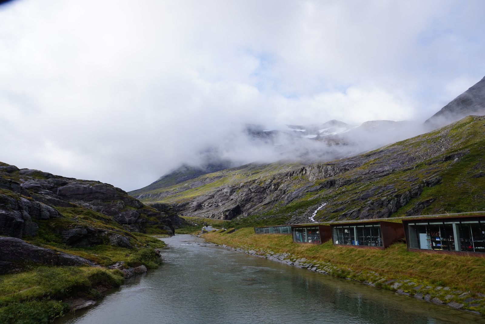 Mountain slopes above a river and grass-roofed buildings in fog, Trollstigen