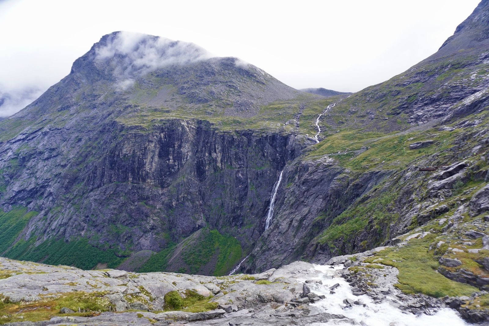 Rocky slopes above waterfalls and a stream under low clouds, Trollstigen