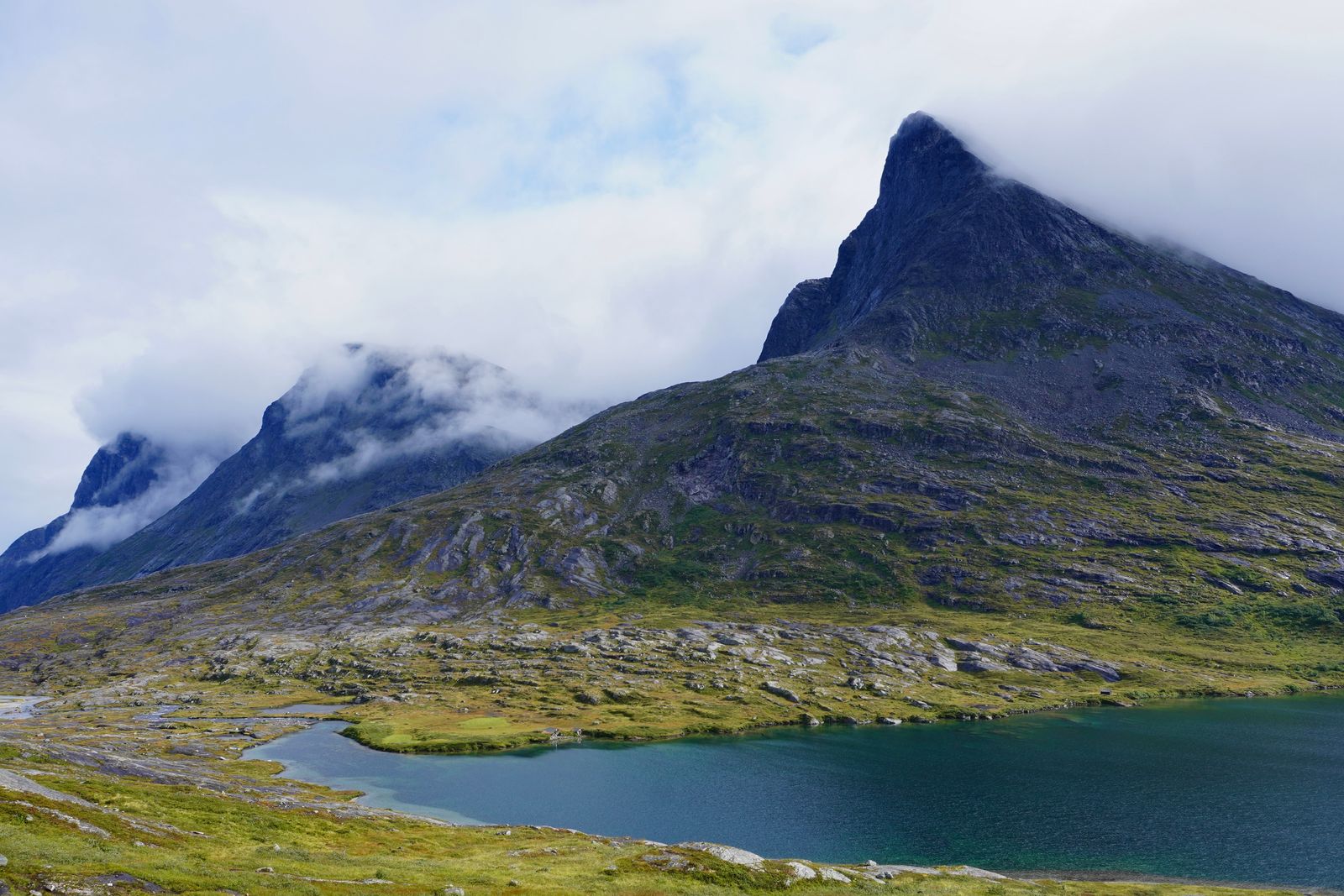 Rocky peaks above a blue-green lake under low clouds, Trollstigen