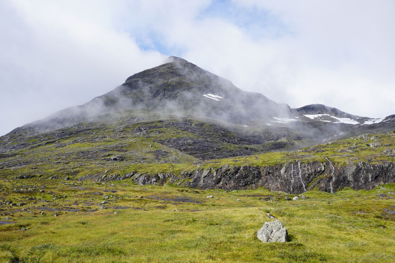 Rocky mountain above grassy slopes and waterfalls in fog, Trollstigen