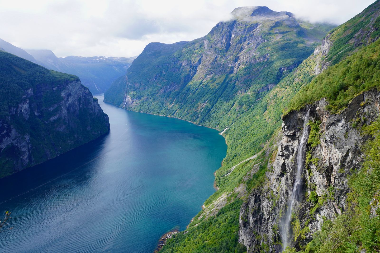 Waterfall dropping down a rocky cliff beside a blue fjord, Geiranger