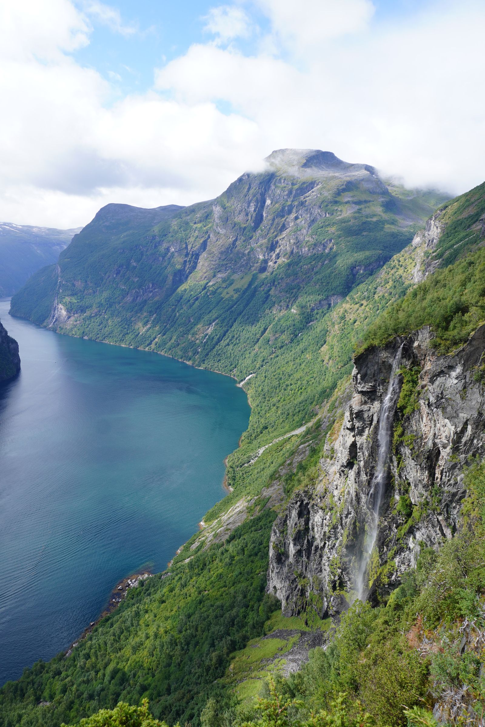 Waterfall dropping down a rocky cliff beside a blue fjord, Geiranger