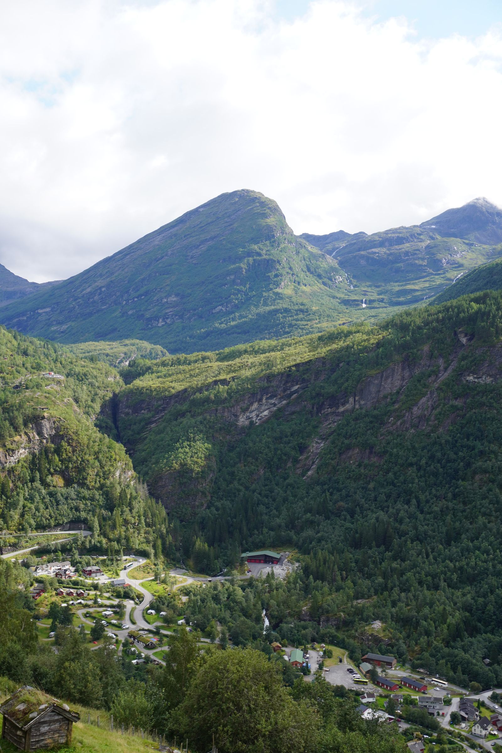 Green mountain above winding roads and a wooden hut, Geiranger