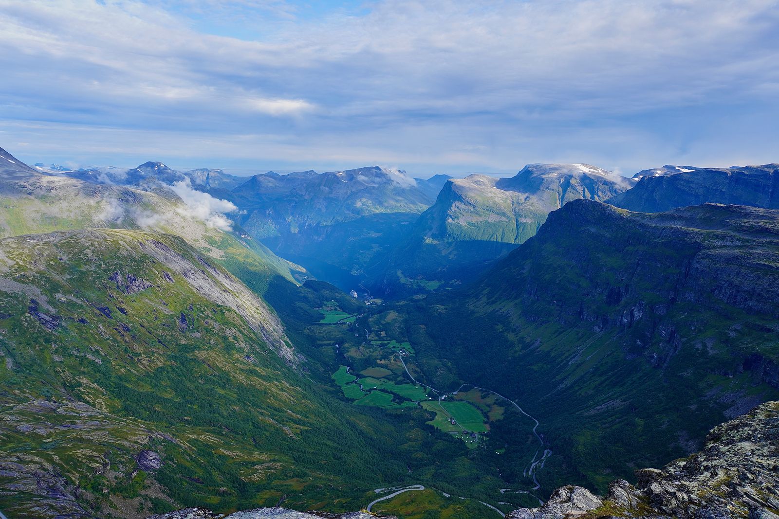 Mountains above valley fields and a winding road under clouds, Geiranger