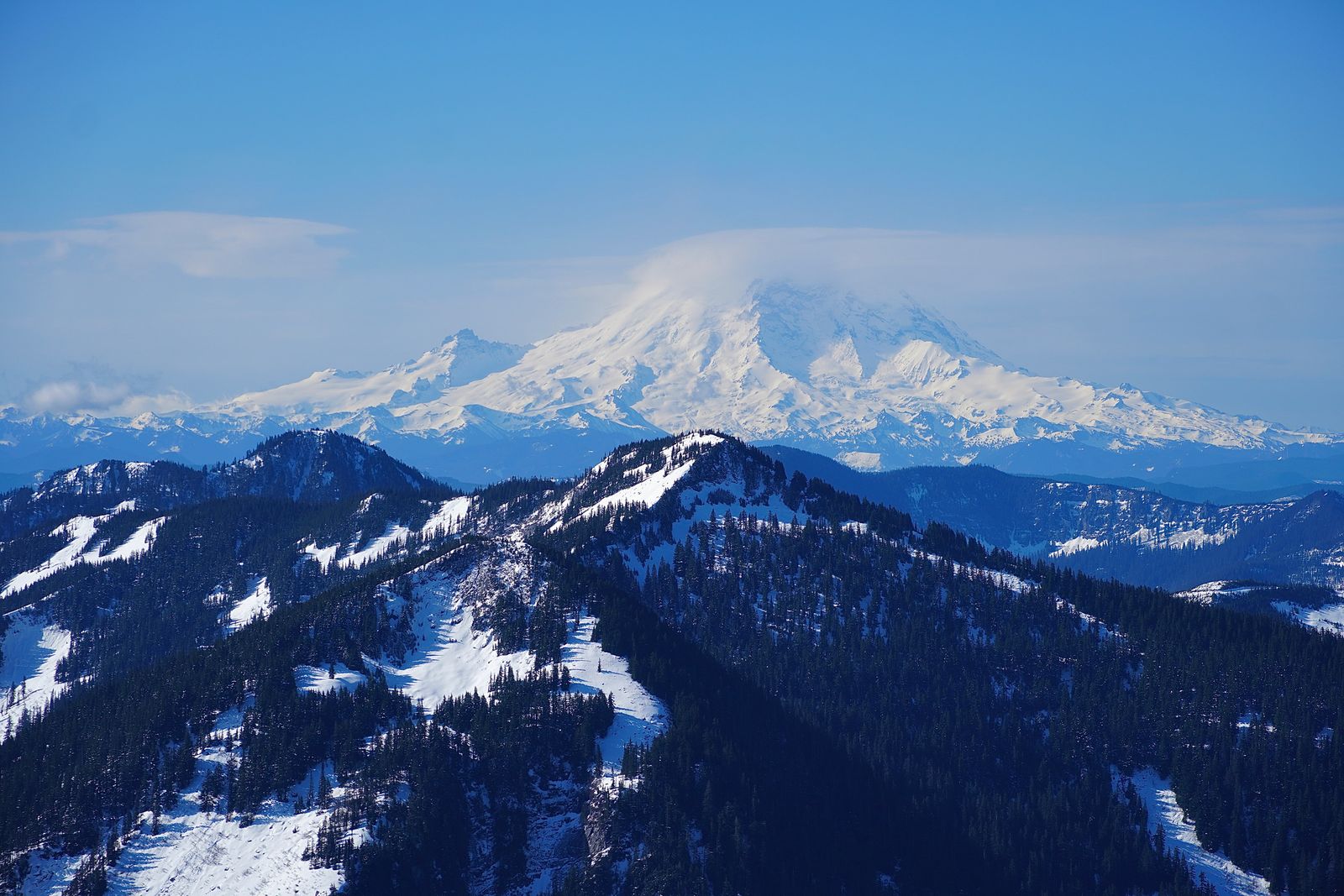 Snow-covered mountain rising behind snow-covered forested ridges with clouds covering the summit, Western Washington
