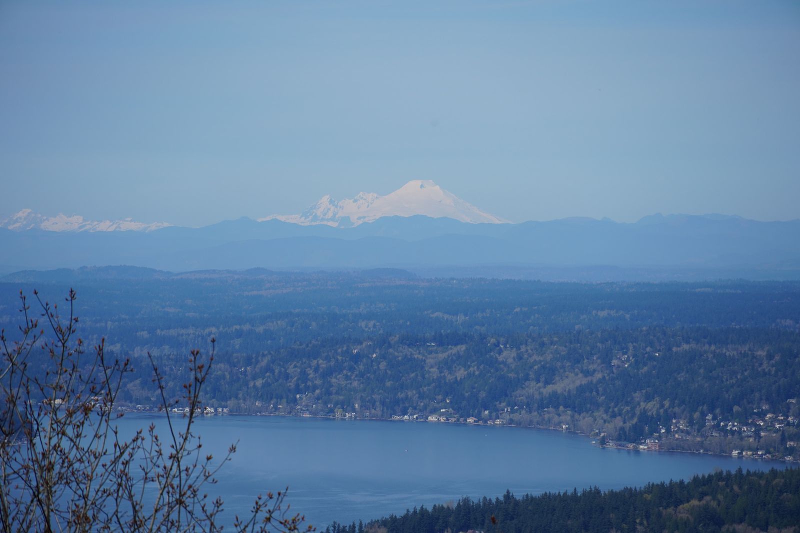 Snow-covered peak beyond wooded hills and a lake in haze, Western Washington