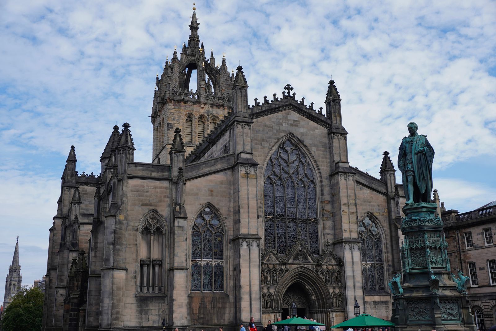 Stone church beyond a green statue and umbrellas, Edinburgh Town