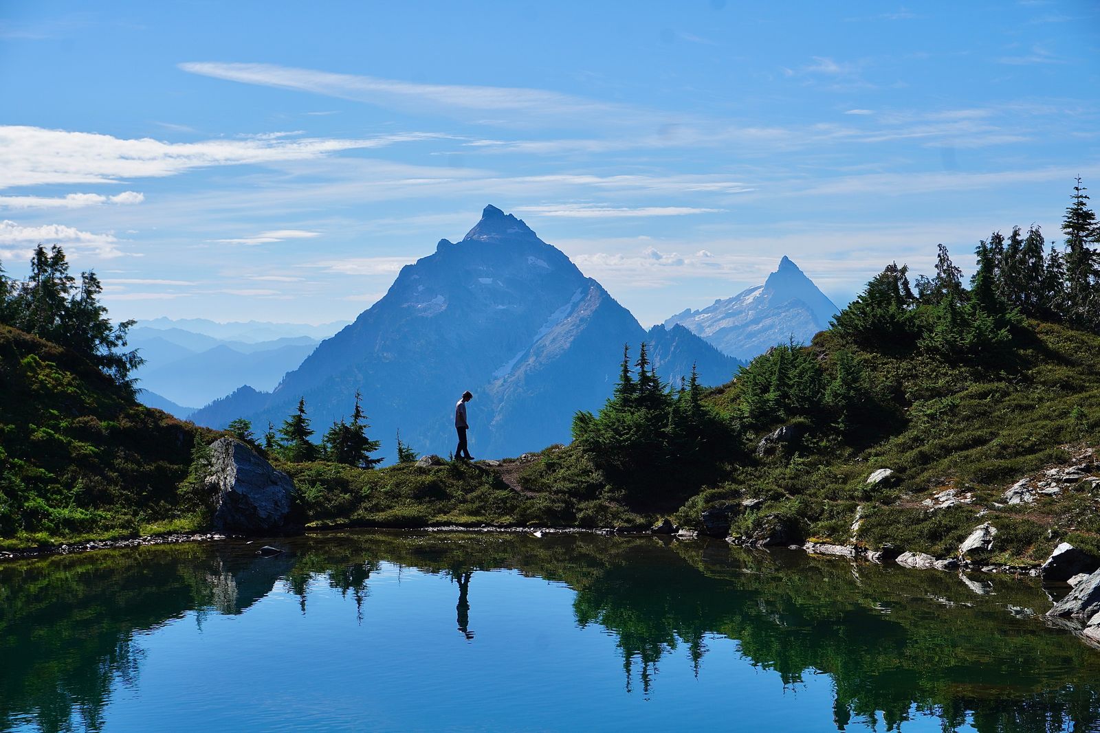 A person reflected in a tarn below rocky peaks, Cascades