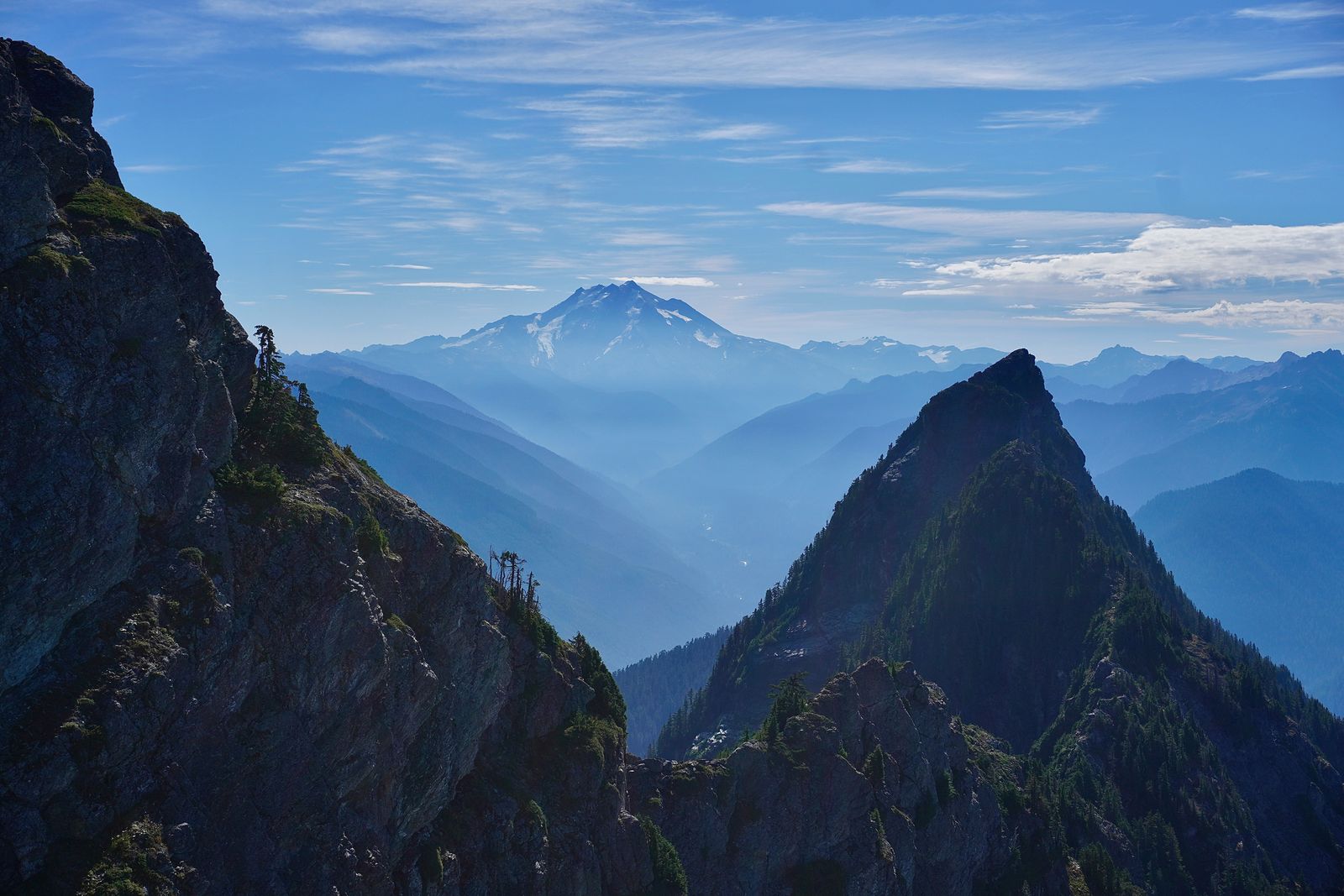 A snow-streaked peak beyond rocky ridges in haze, Cascades