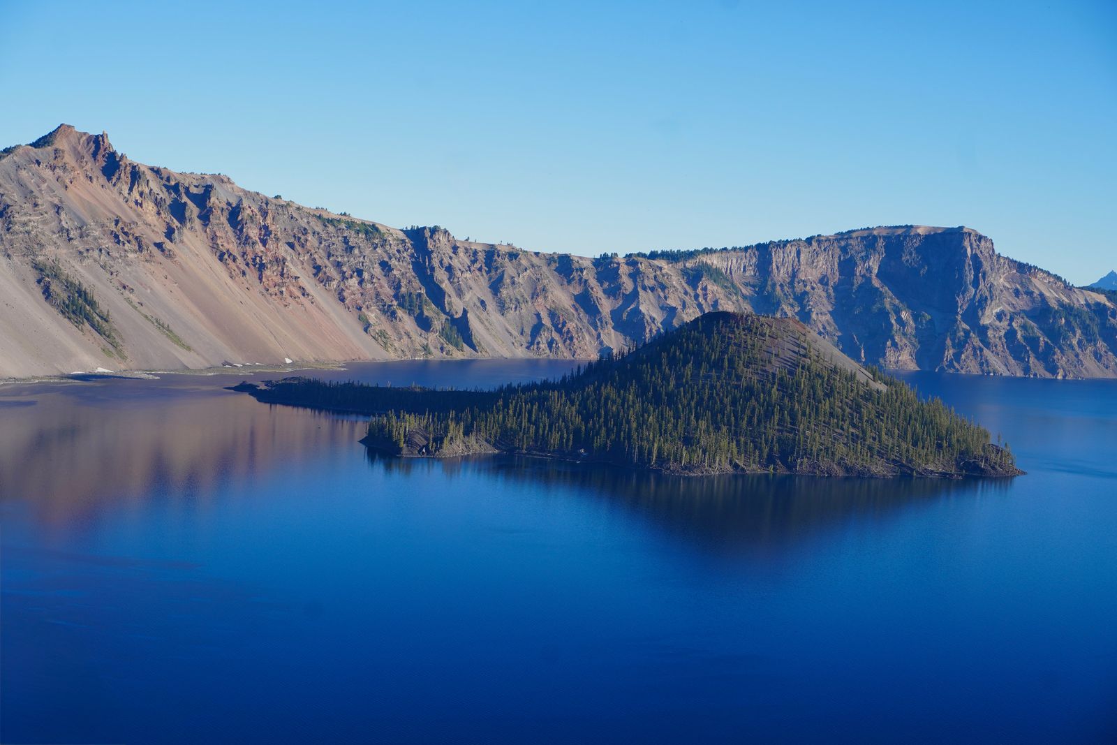 Crater Lake surrounding a wooded island below steep cliffs
