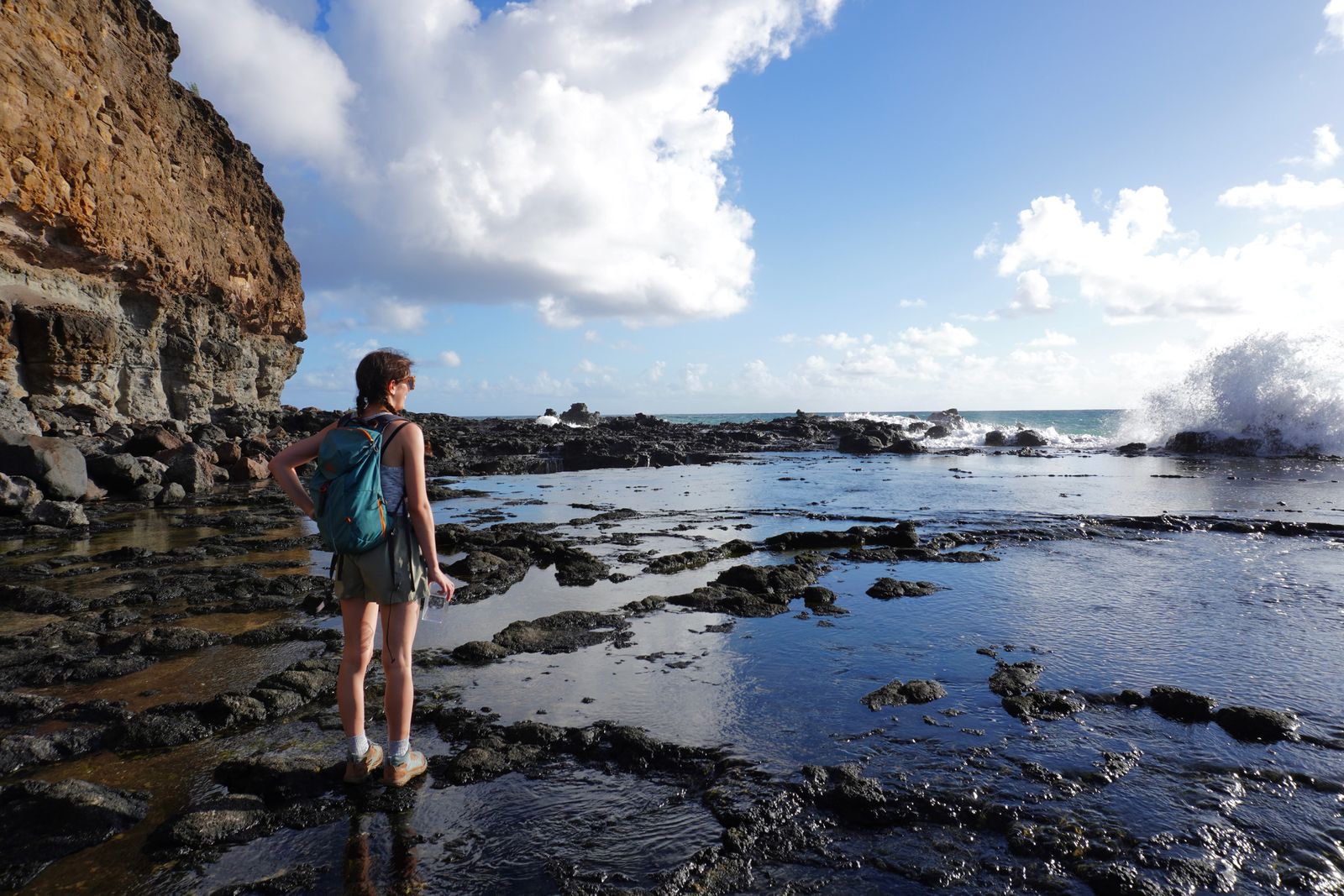 A backpacker on wet rocks beside tide pools and waves, Northern Kauai