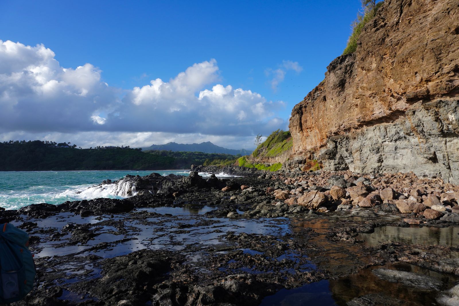 Rocky shoreline with tide pools beneath a layered cliff, Northern Kauai