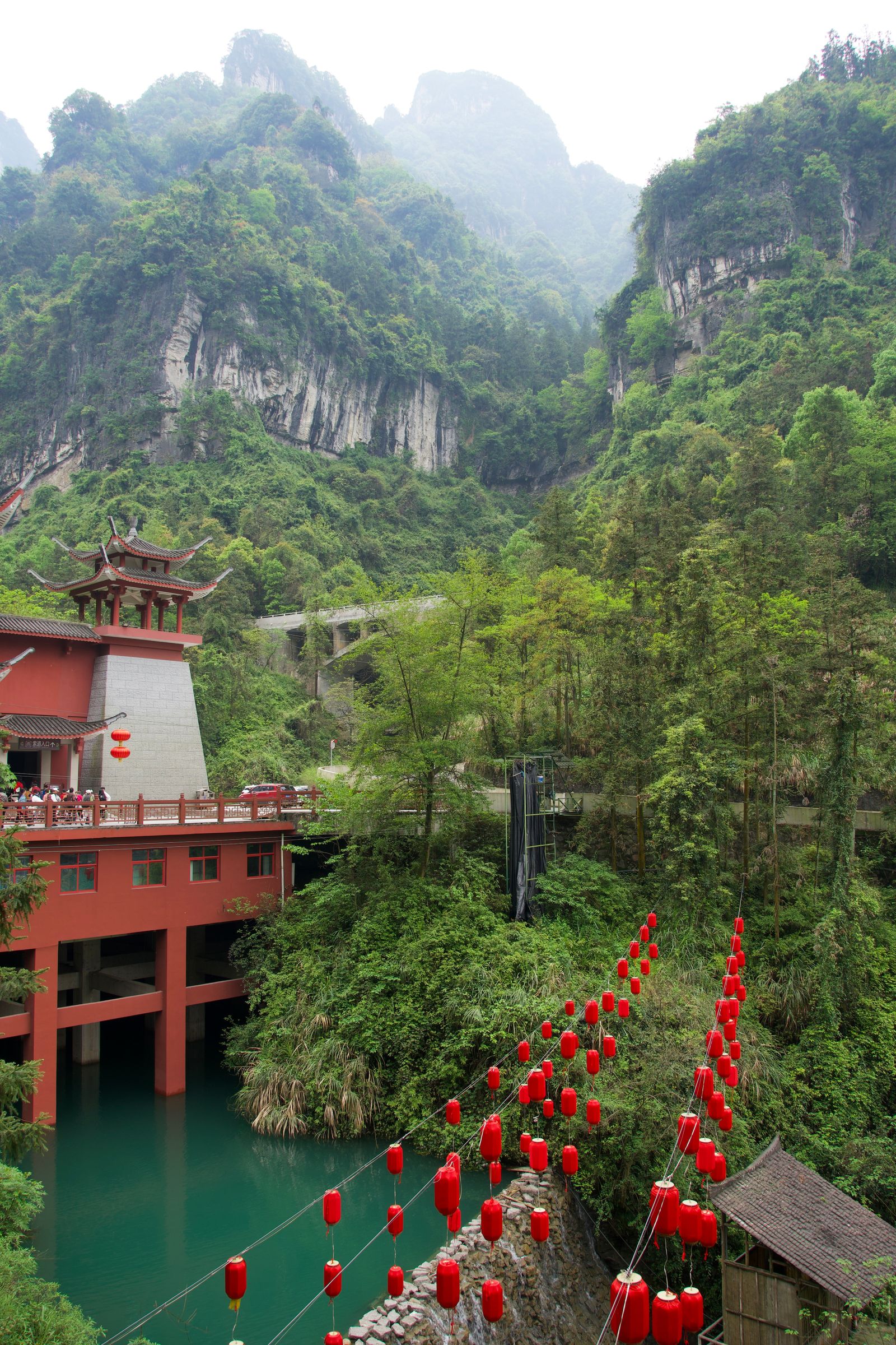 Forested cliffs above red buildings and lanterns in mist, Zhangjiajie