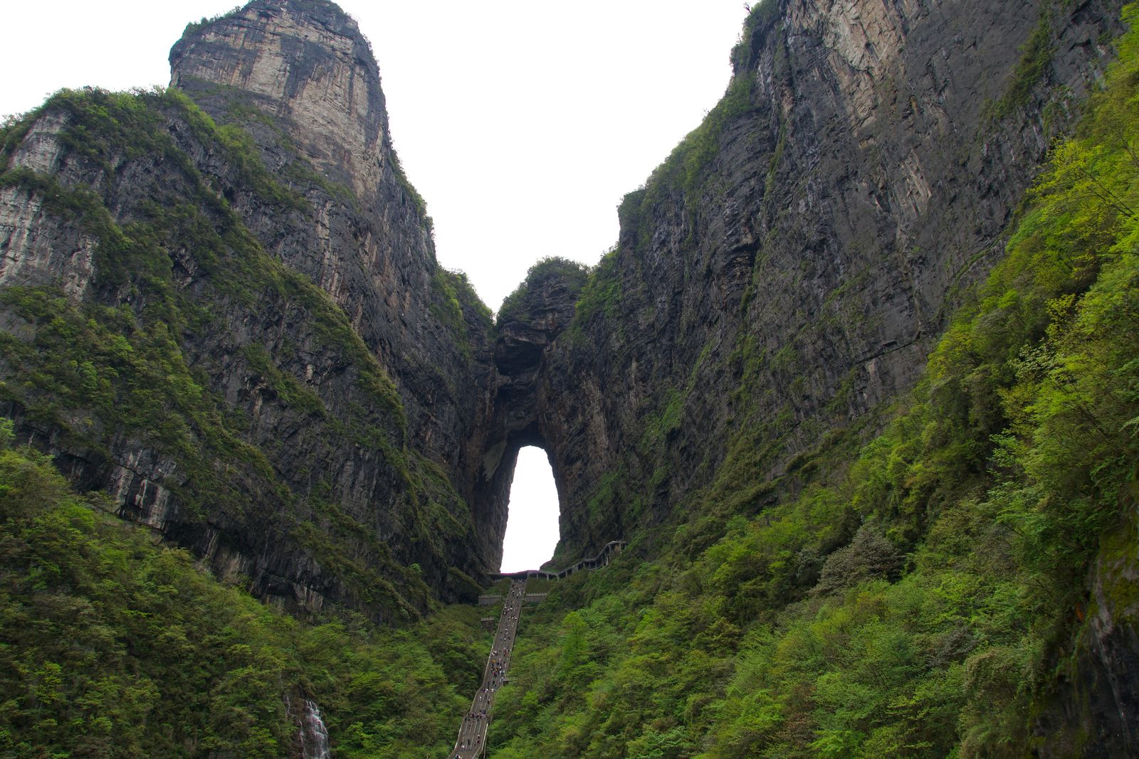 A rock arch above a long staircase between wooded cliffs, Zhangjiajie