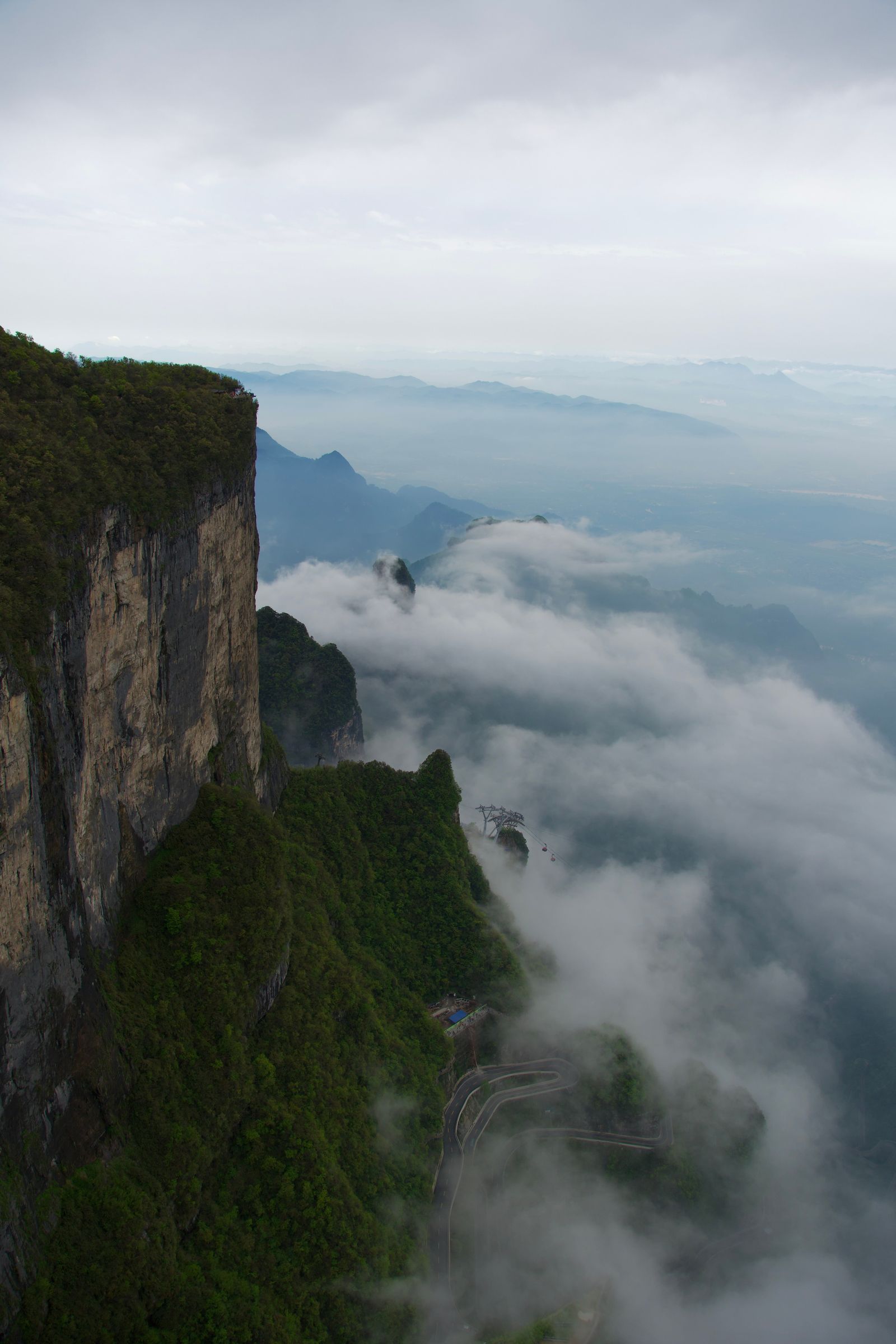 Forested cliffs above a winding road in low cloud, Zhangjiajie